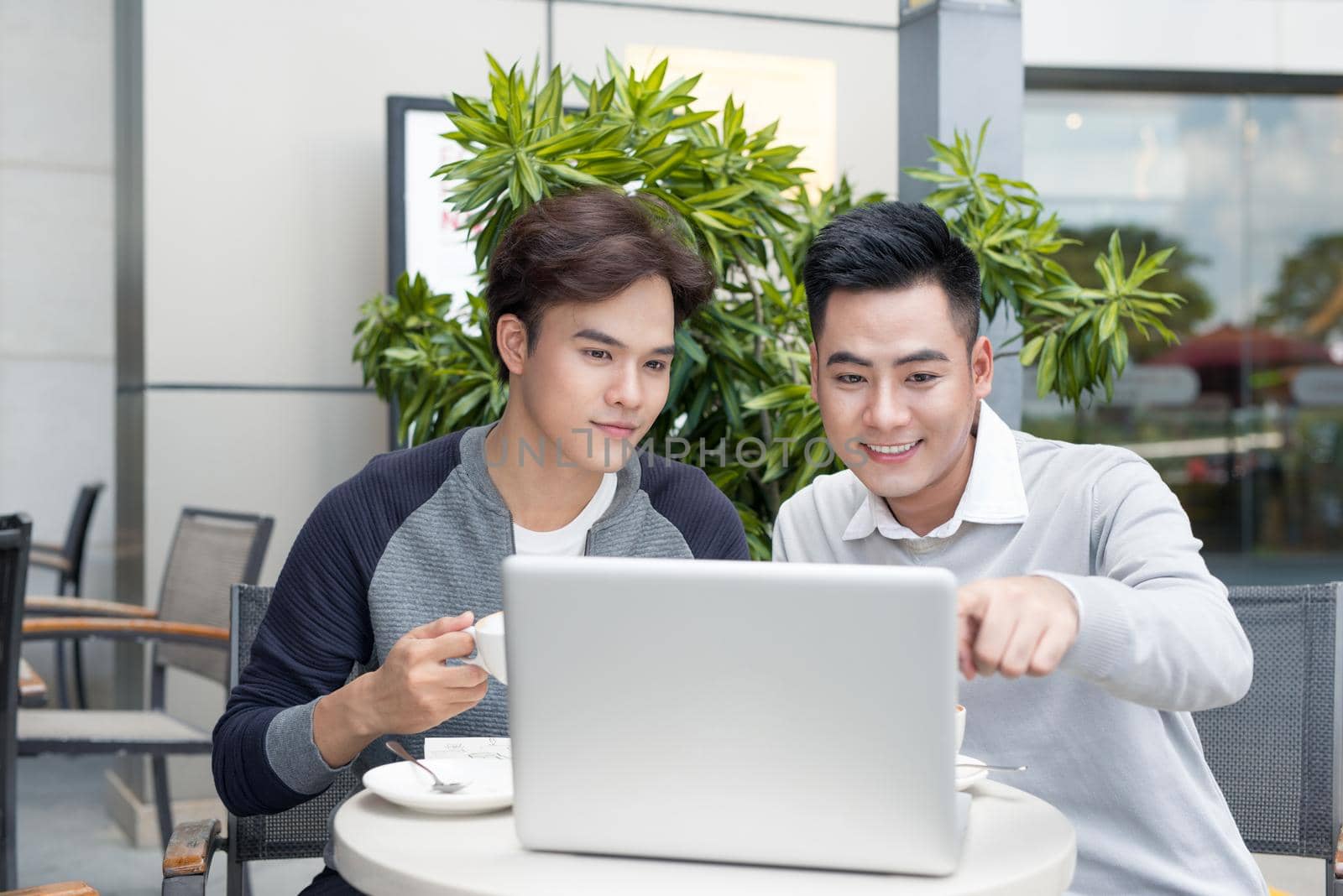 Man showing document to his colleague while they are drinking coffee in city by makidotvn