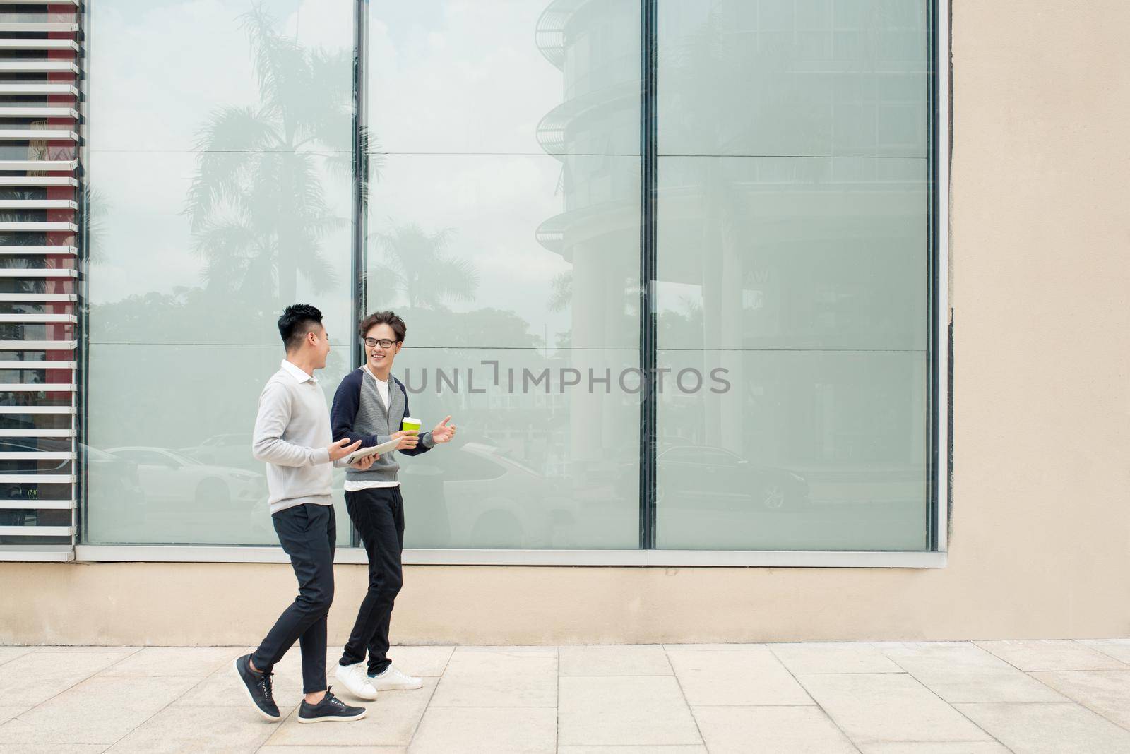 Two asian men talk and use smart phone outside the building