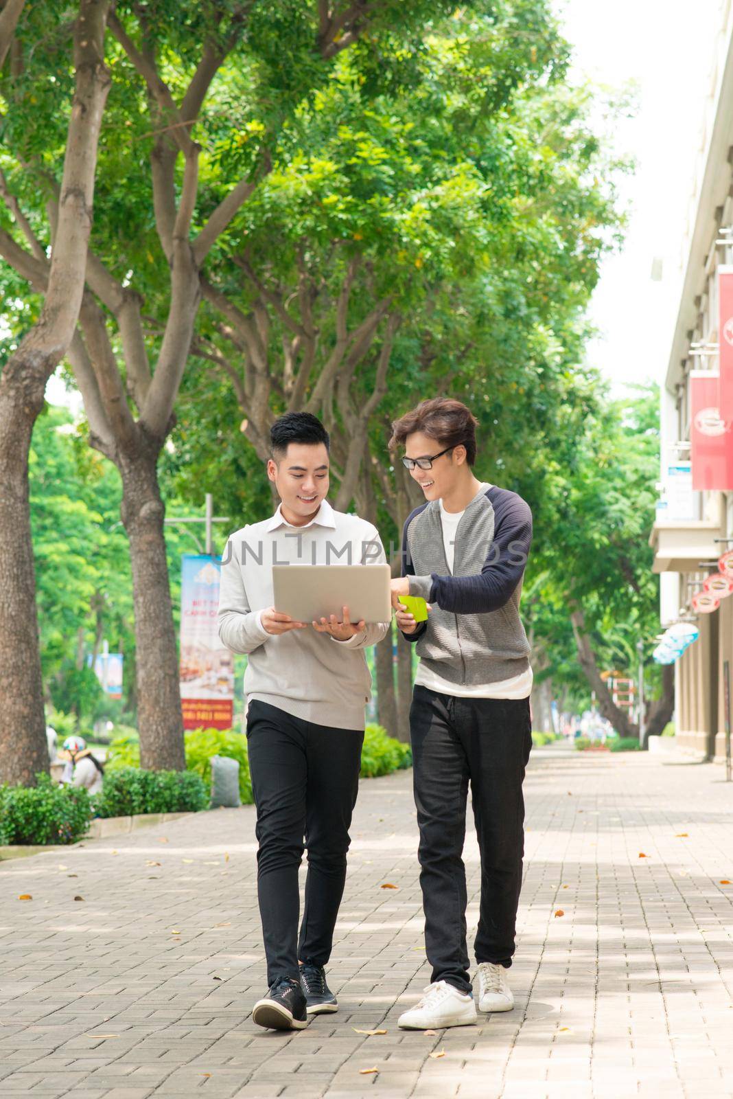 Two smiling young businessmen walking and talking in the city by makidotvn