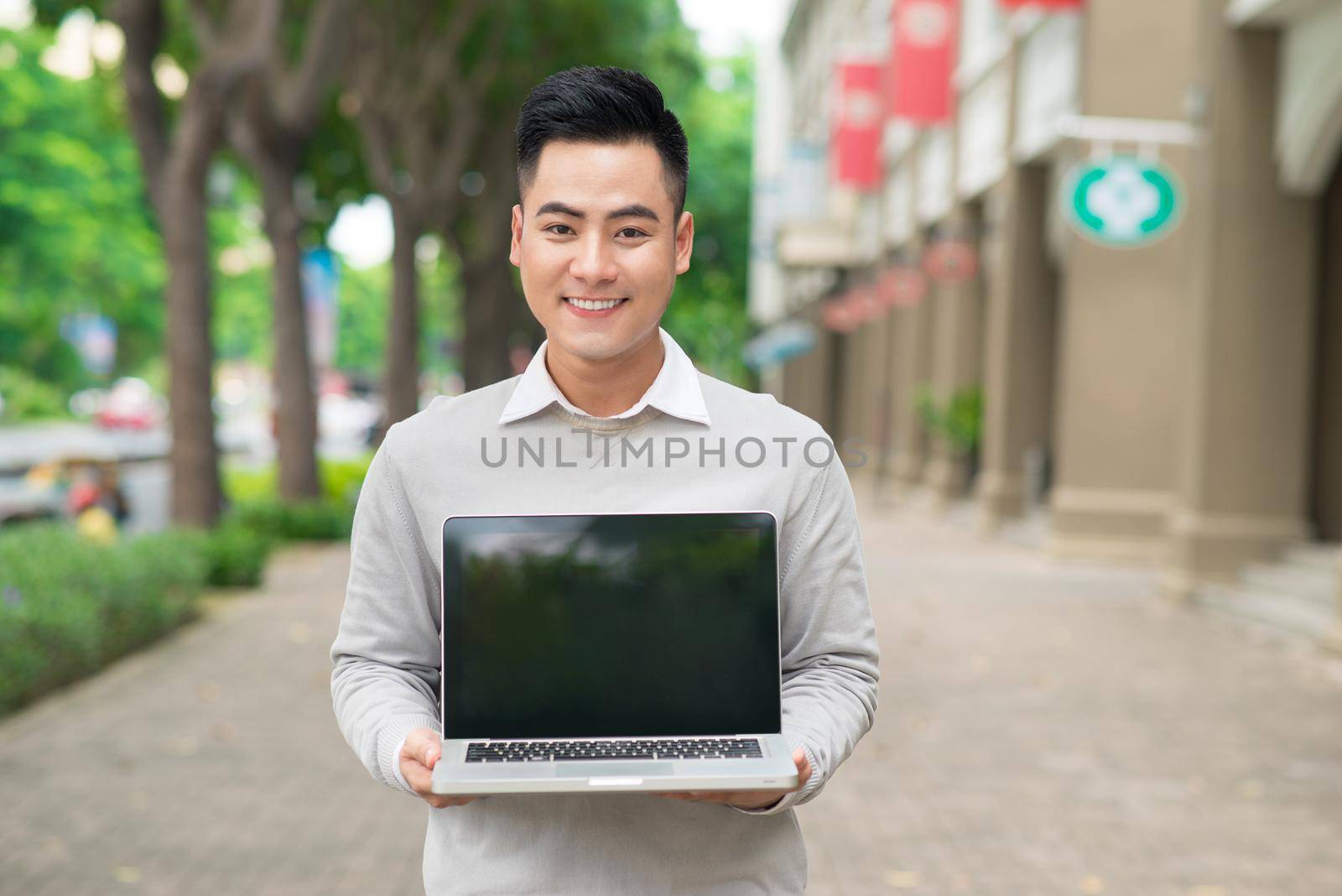 Young business man holding and showing the screen of laptop
