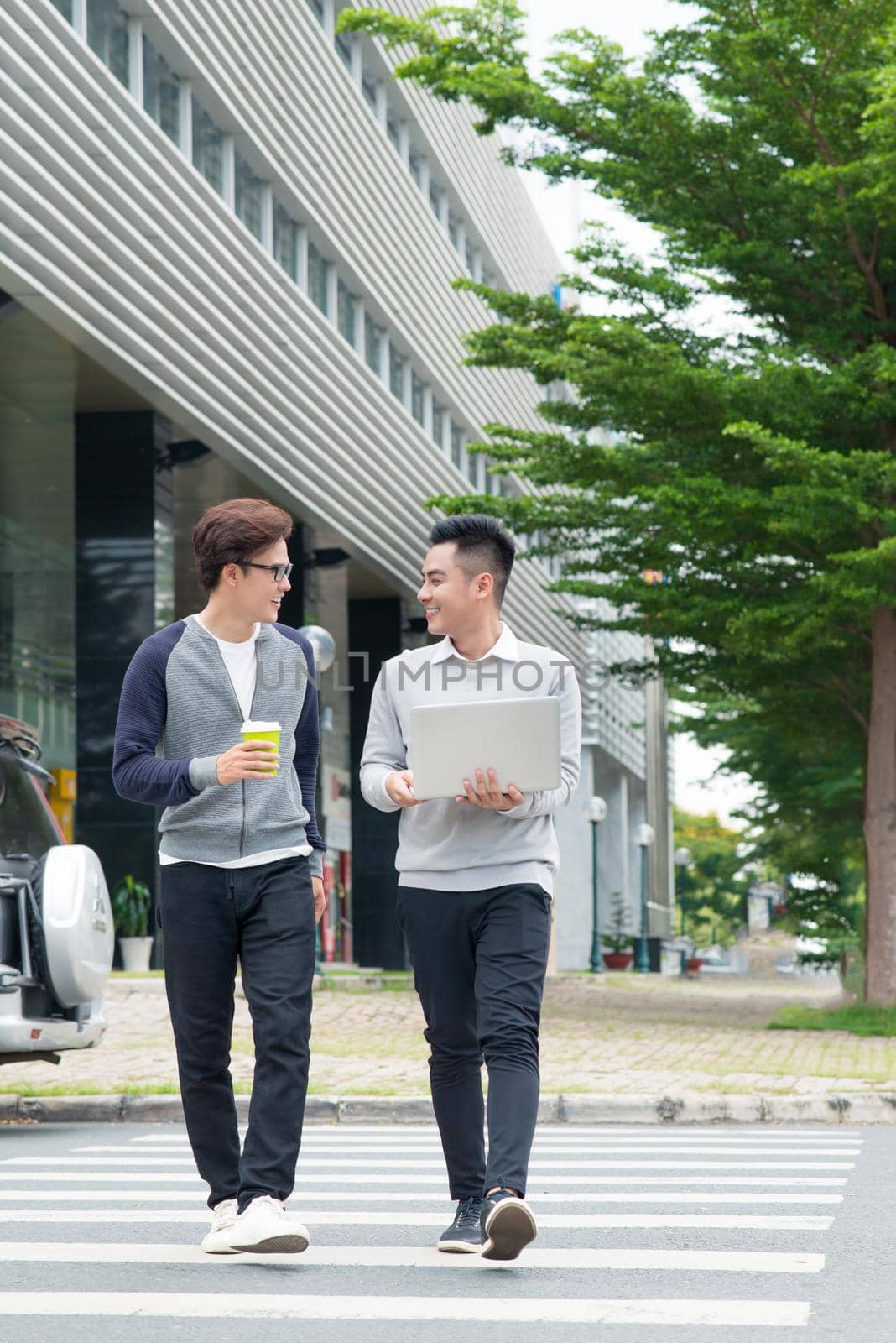Two smiling young businessmen walking and talking in the city by makidotvn