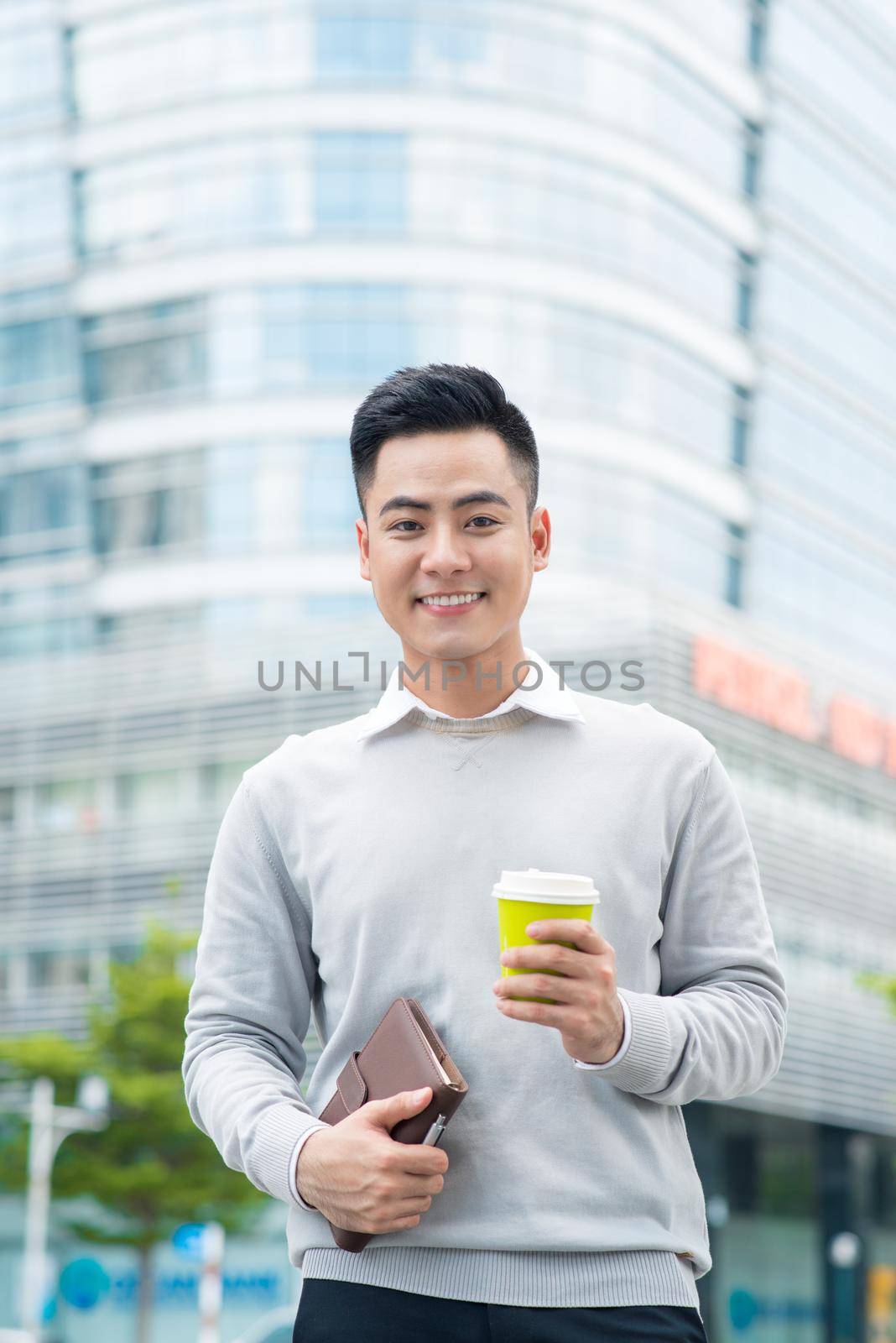 Portrait of a handsome man standing with coffee on city street