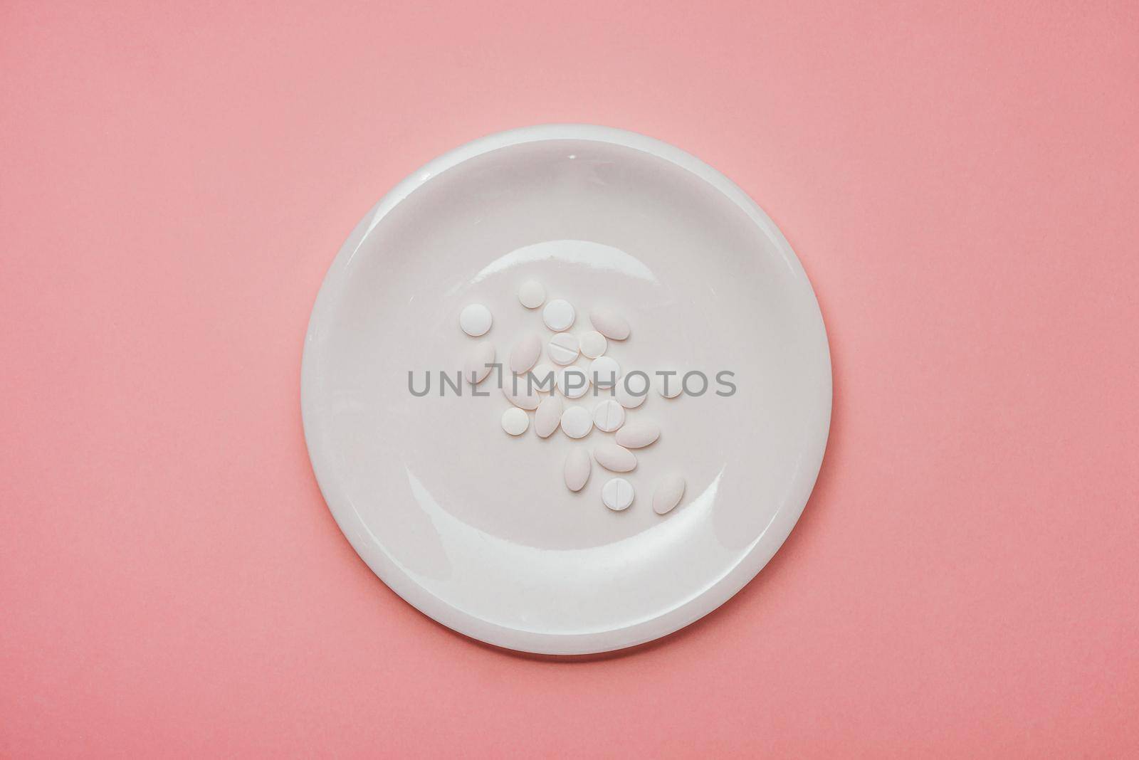 Pills served as a healthy meal. Drug capsule on white plate on pink background by makidotvn