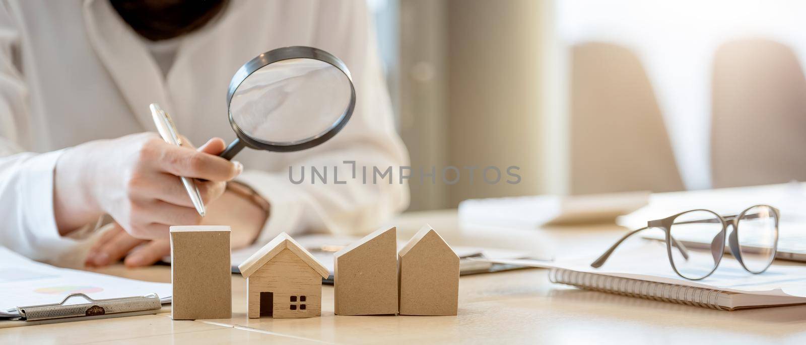 Looking for real estate agency, property insurance, mortgage loan or new house. Woman with magnifying glass over a wooden house at her office by nateemee