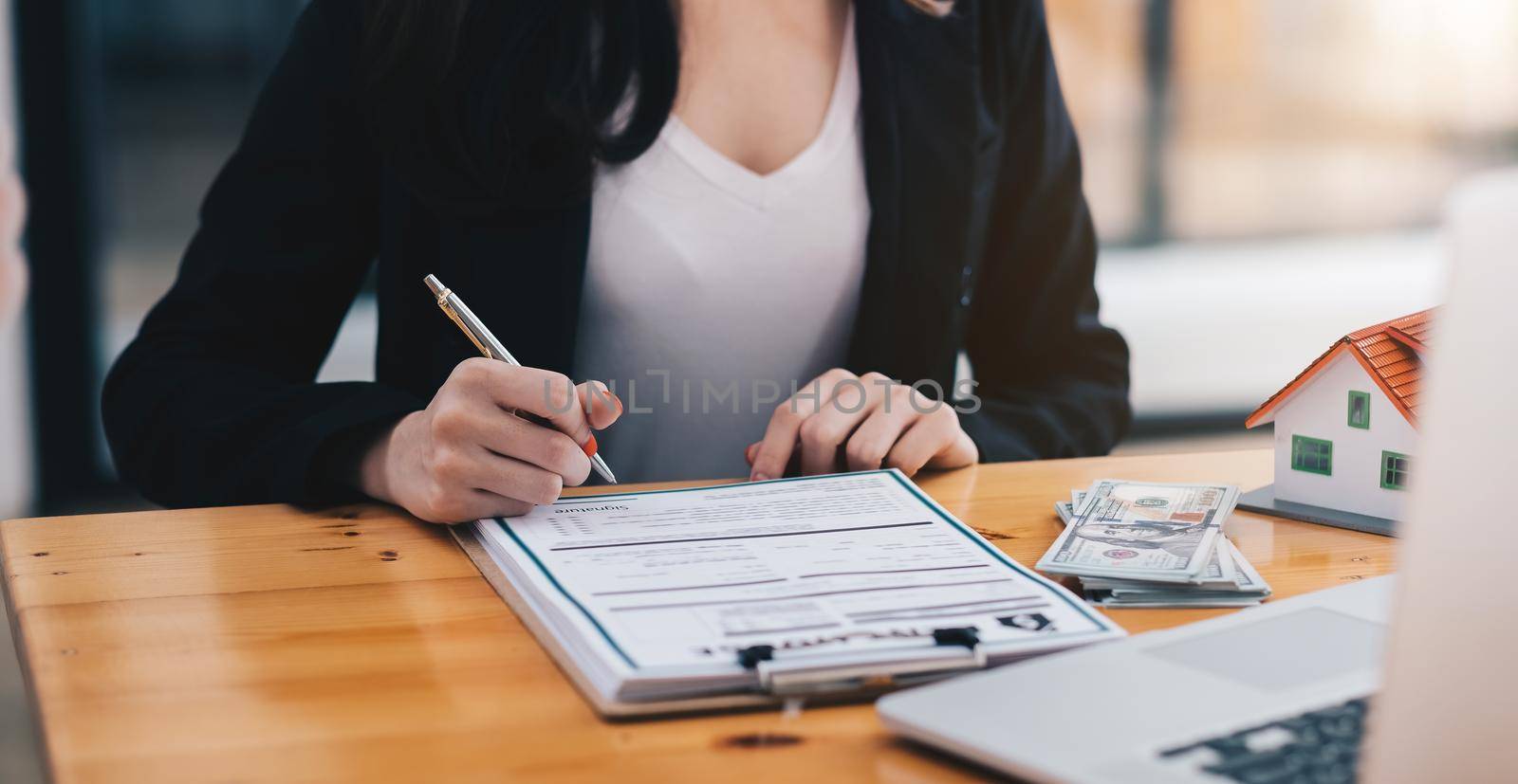 close-up view hands of businesswoman signing leasing home documents and house model on wooden desk by nateemee