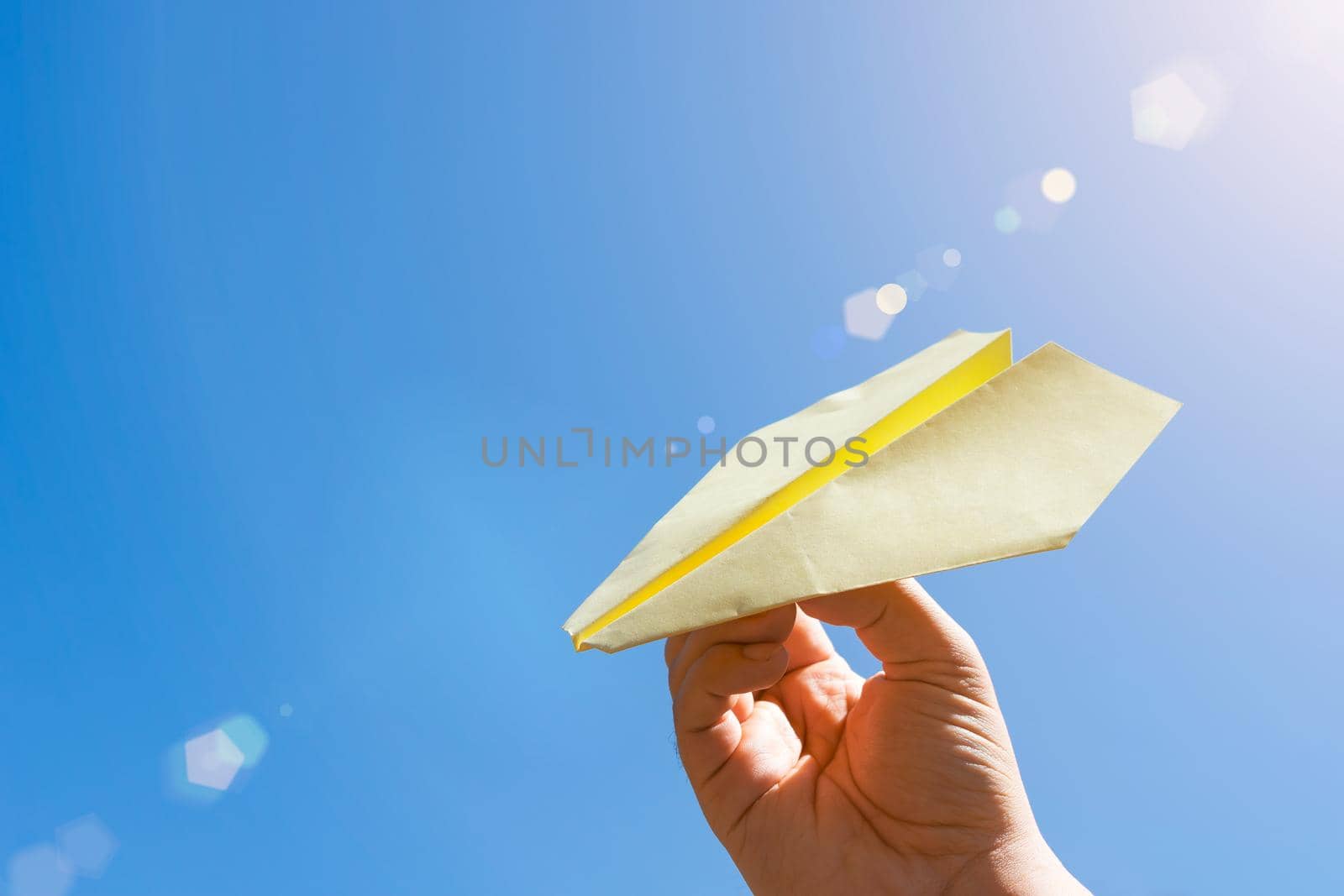 Children play with a paper airplane against a background of blue sky and warm summer sun glare. Hobby to fold origami paper