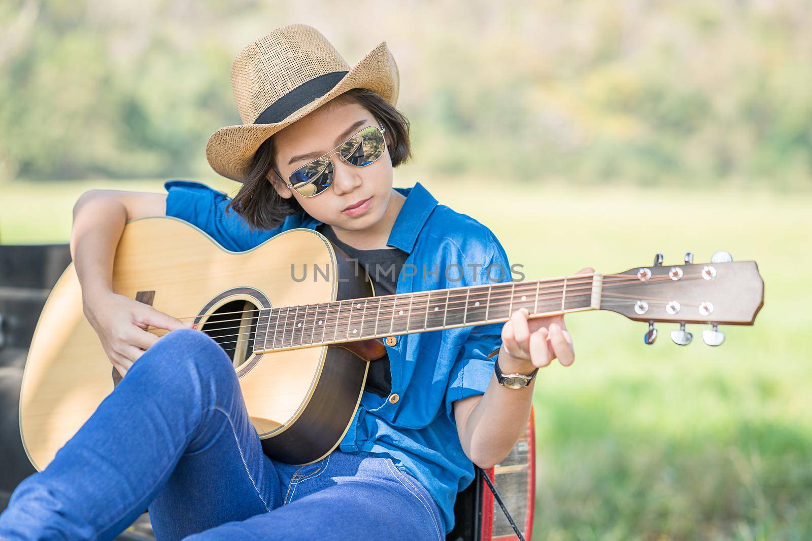 Young asian women short hair wear hat and sunglasses playing guitar ,sit on pickup truck in countryside Thailand