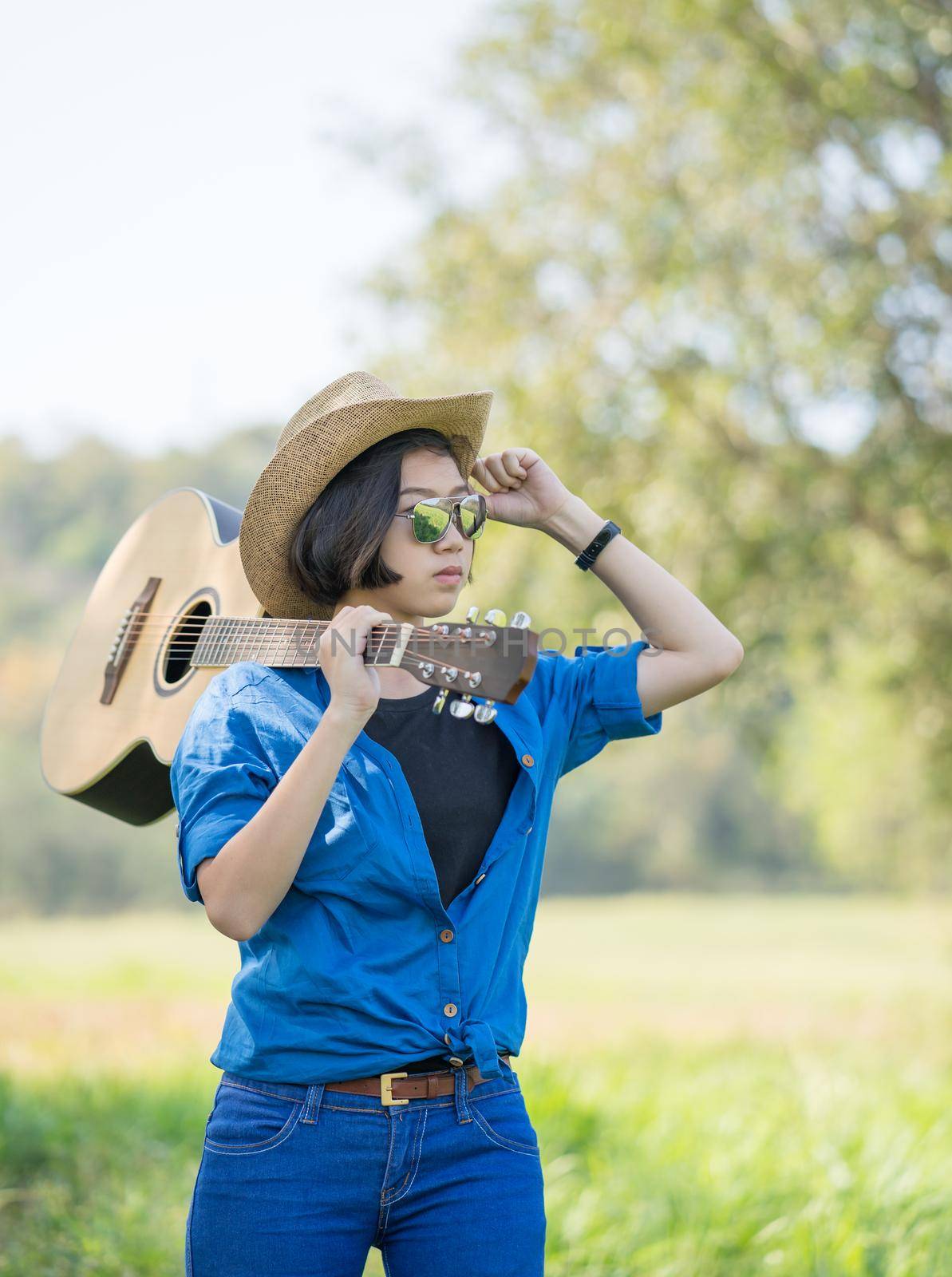 Woman wear hat and carry her guitar in grass field  by stoonn