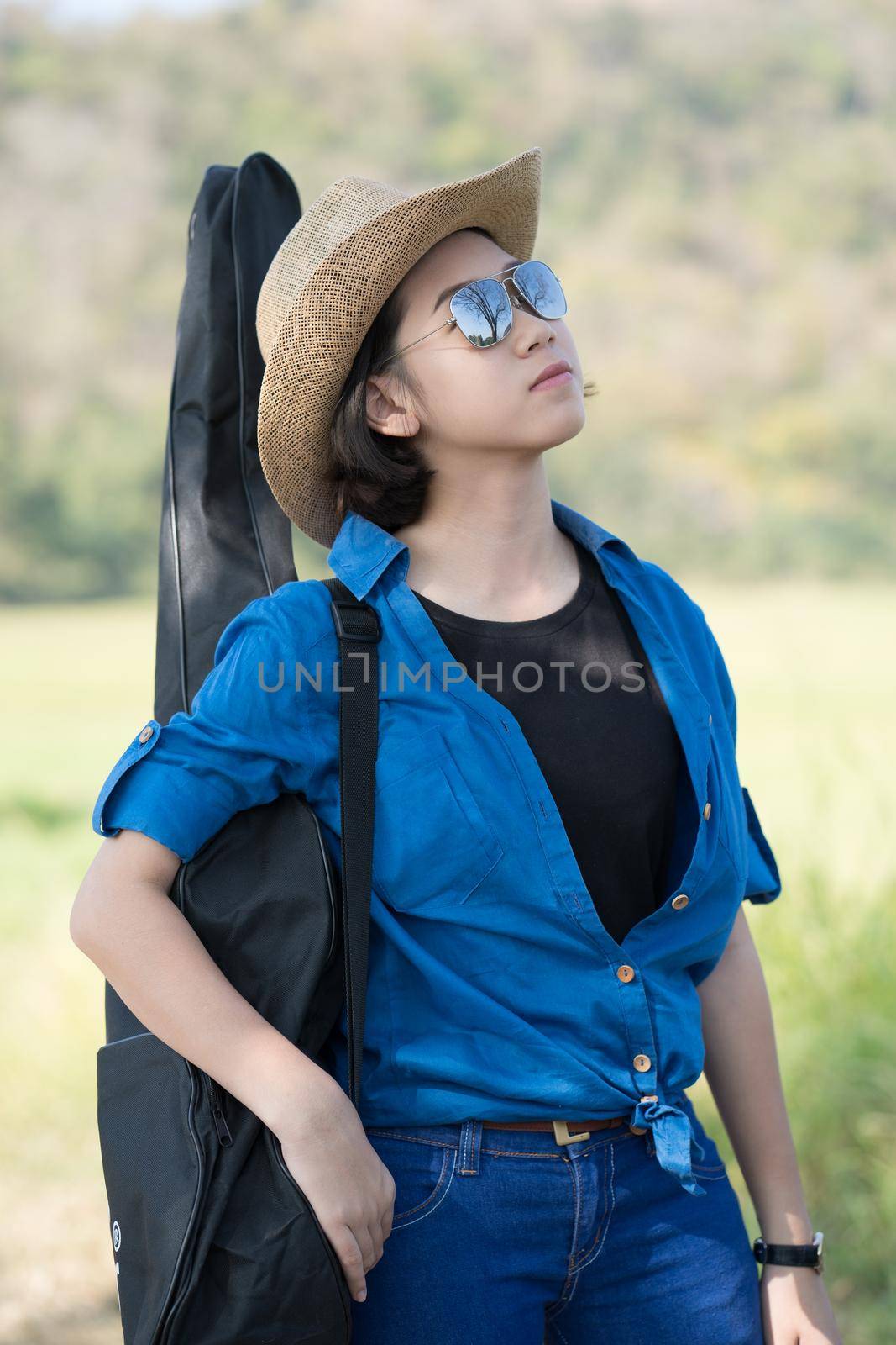 Young asian woman short hair wear hat walking and carry her guitar bag along in countryside Thailand