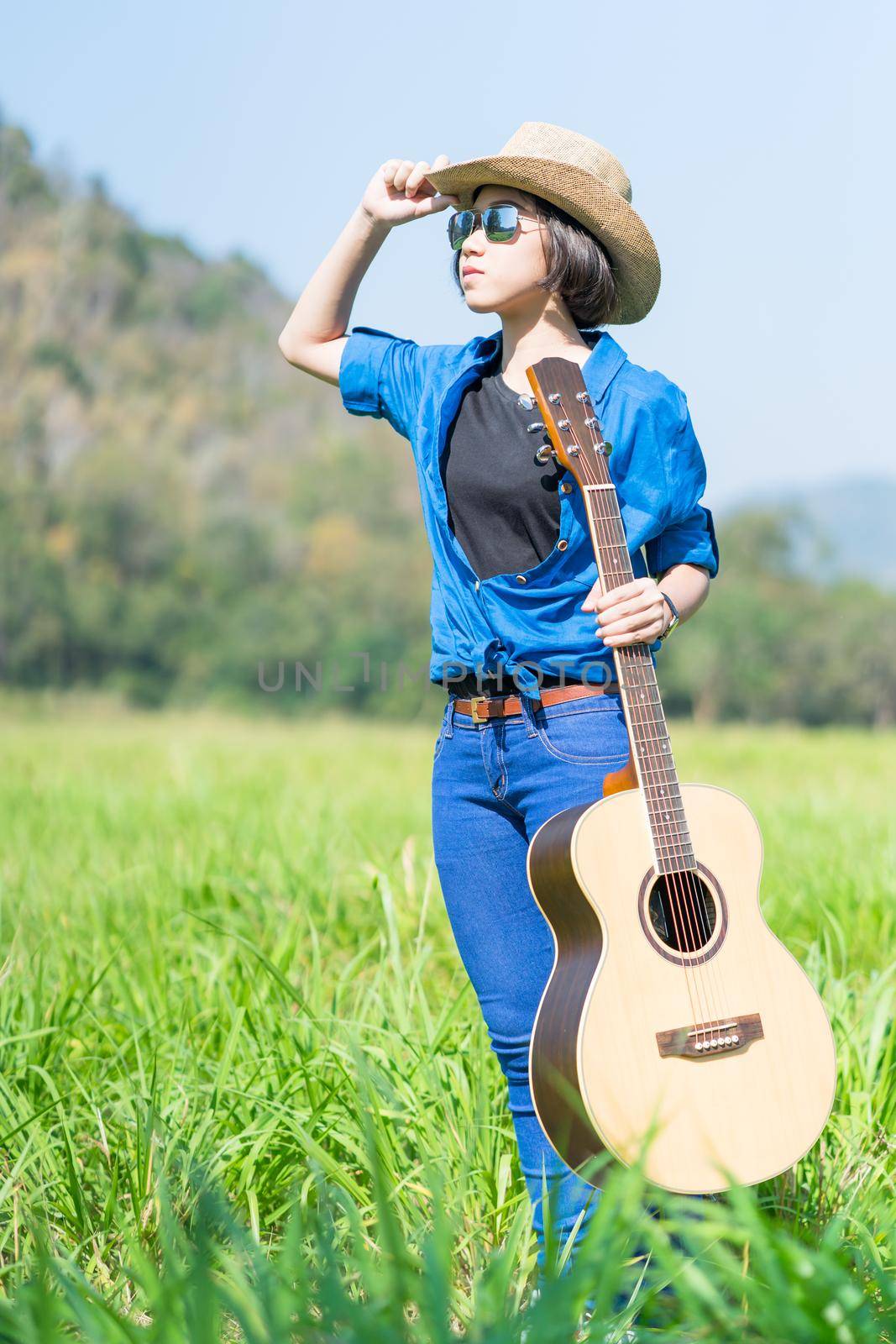 Woman wear hat and carry her guitar in grass field  by stoonn