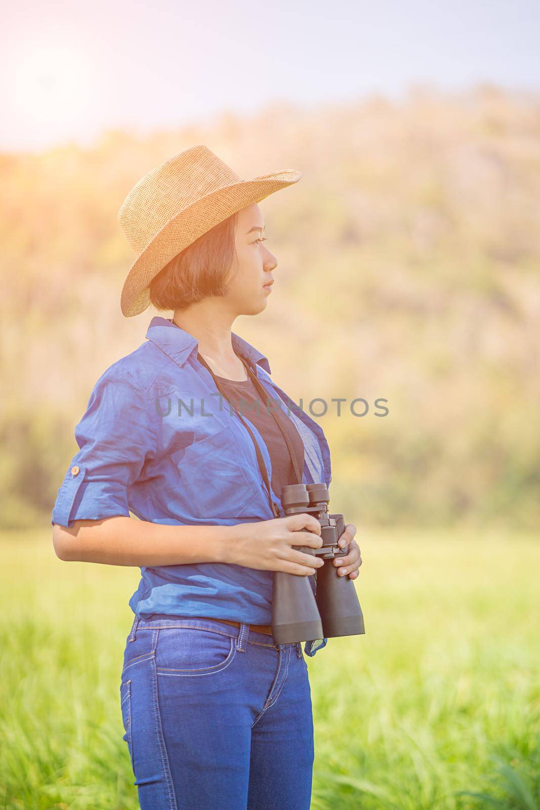 Young asian woman short hair wear hat and hold binocular in grass field countryside Thailand