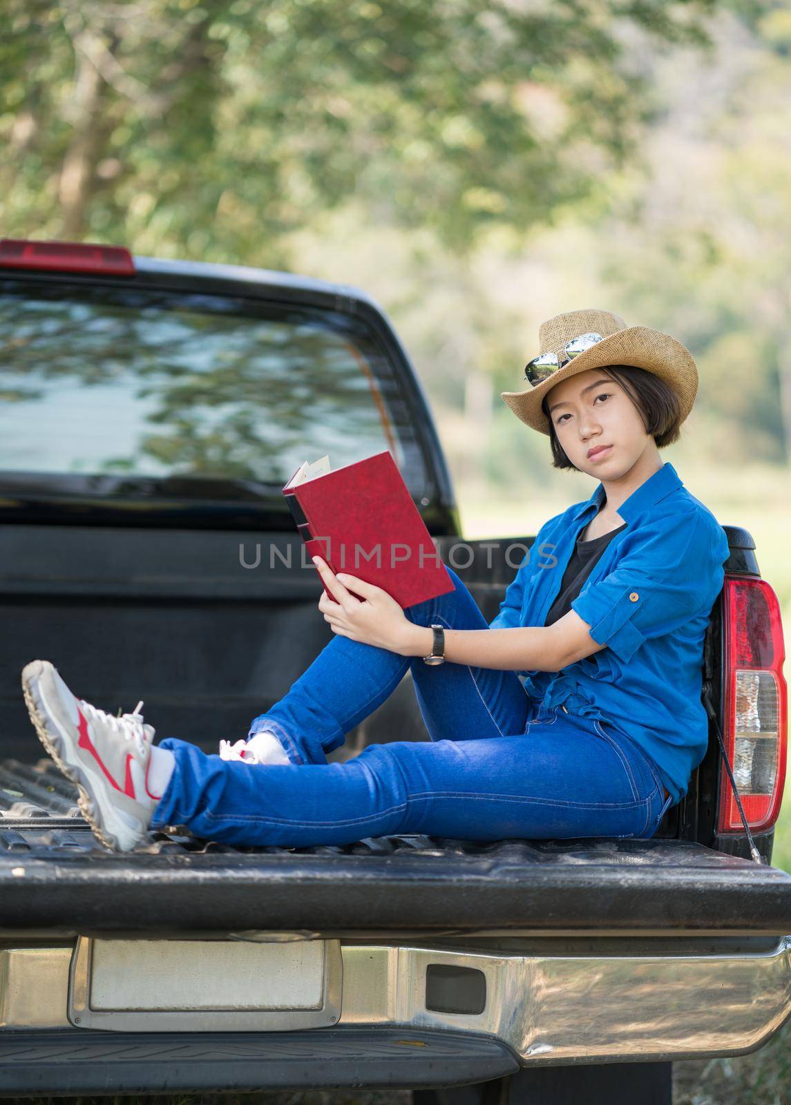Young asian women short hair wear hat and sunglasses read a book ,sit on pickup truck in countryside Thailand