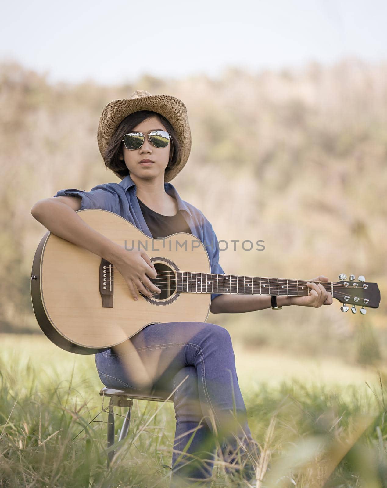 Women short hair wear hat and sunglasses sit playing guitar in grass field  by stoonn