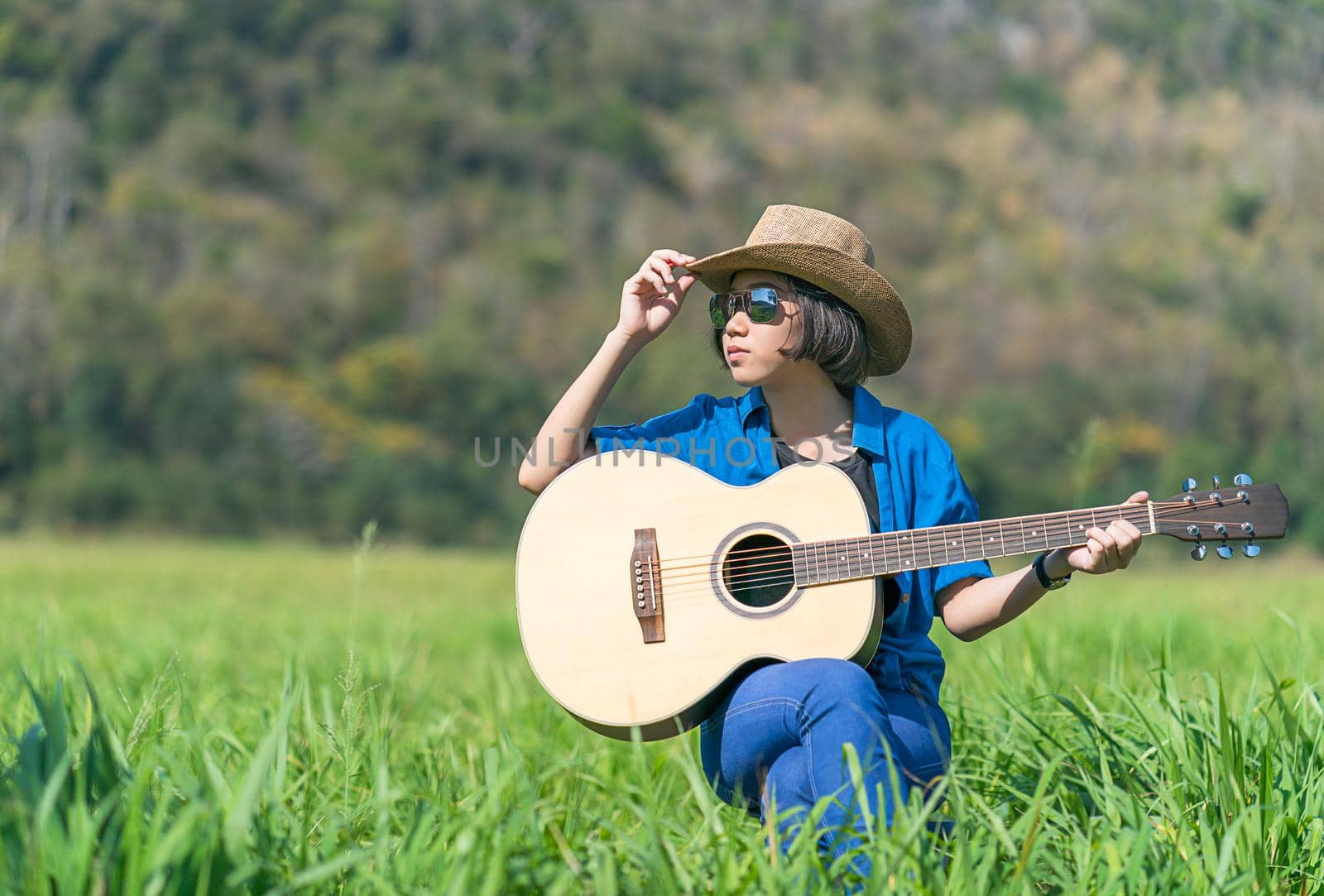 Women short hair wear hat and sunglasses sit playing guitar in grass field  by stoonn