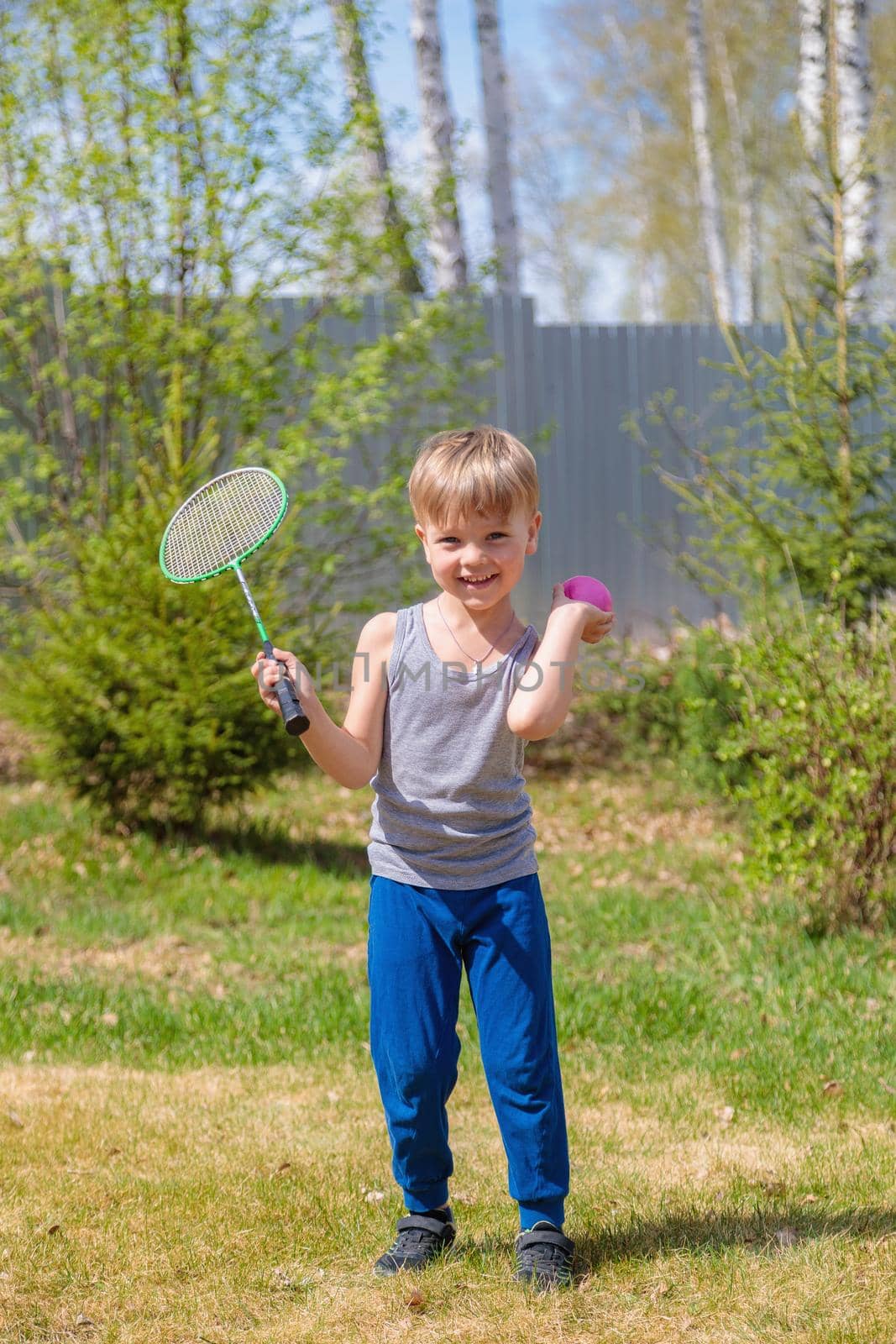 A fair-haired child plays badbinton on the lawn.