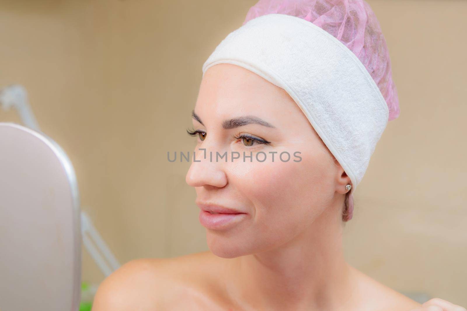A young girl looks at her face in the mirror after a massage. Happy smile.