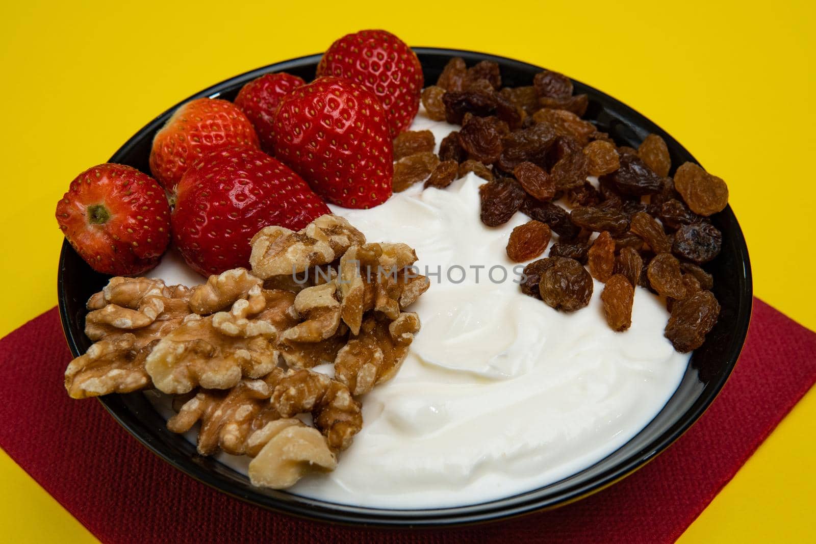 Plain yogurt with strawberries, red napkin, raisins, walnuts and yellow background by xavier_photo