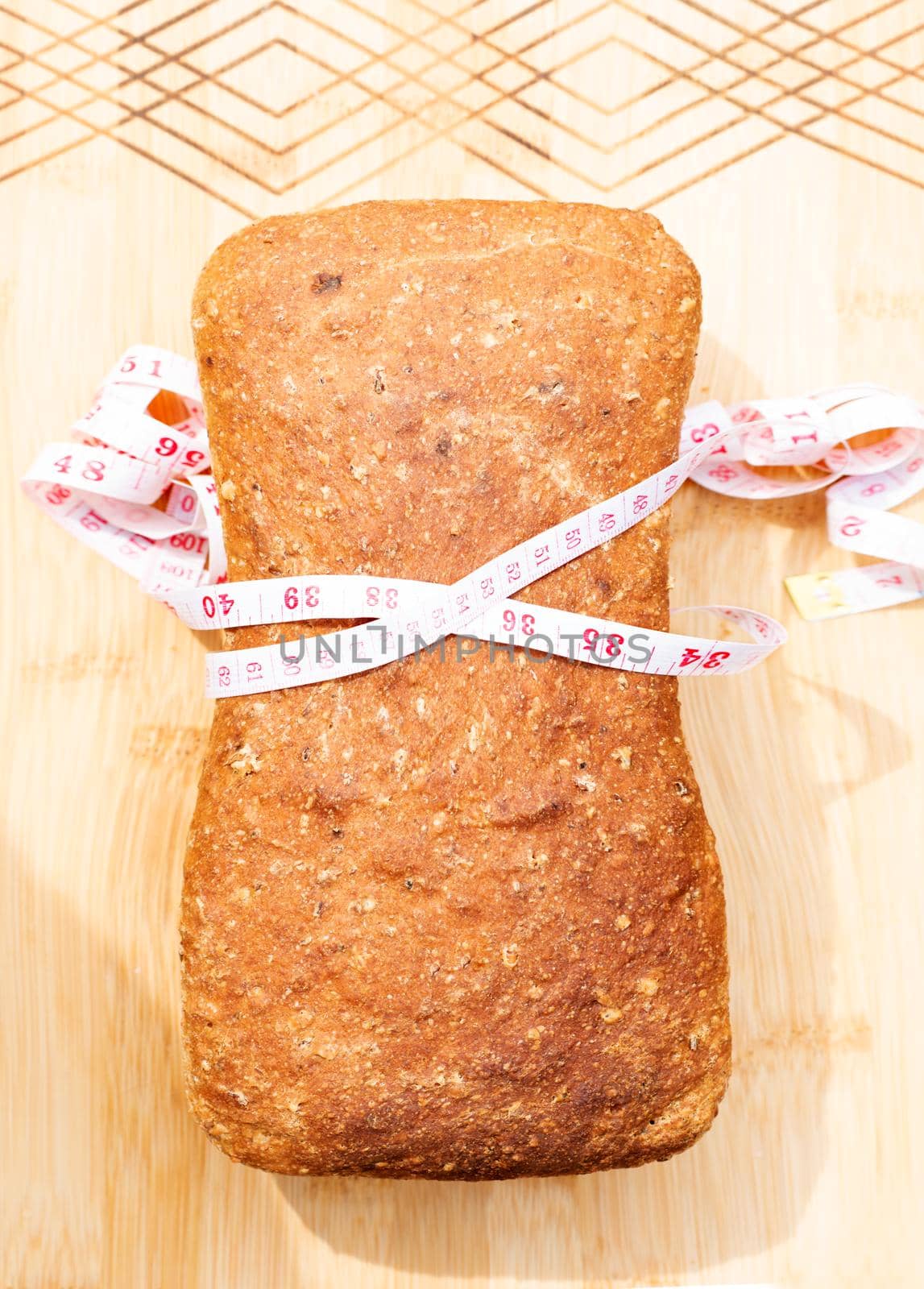whole grain bread wrapped in a measuring tape on a board by Iryna_Melnyk