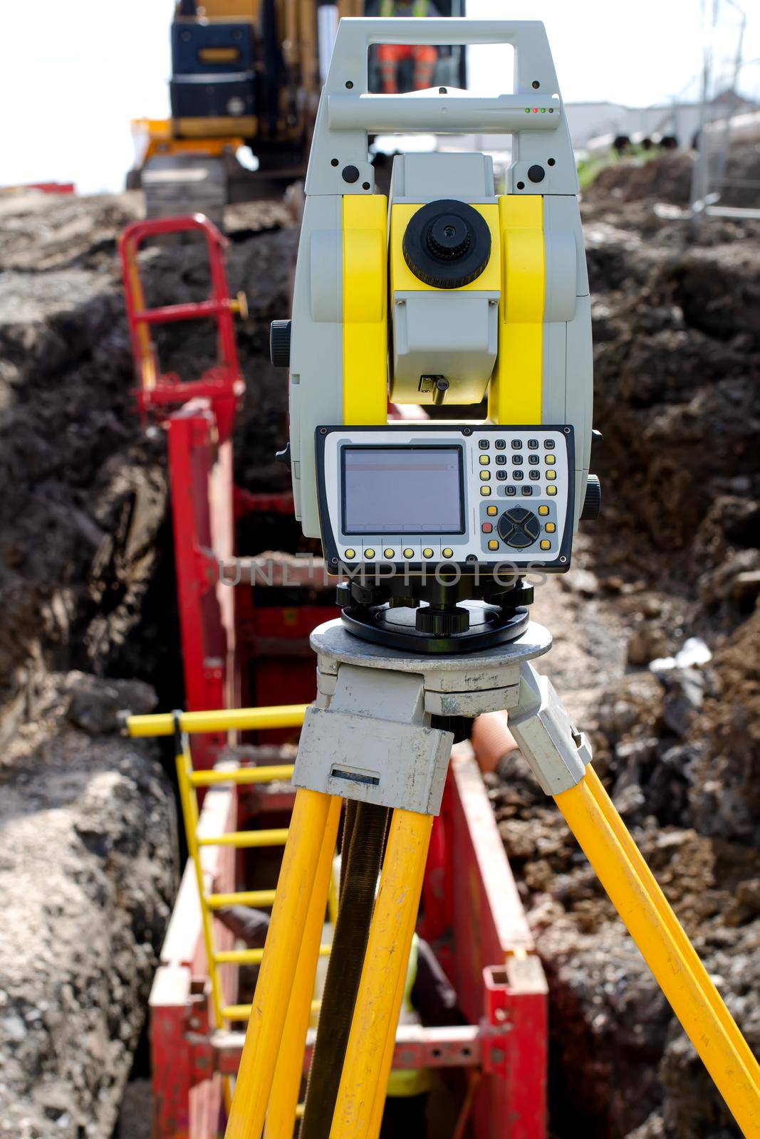 Yellow equipment set out on tripod on building site against cloudless blue sky. Construction site surveying engineering equipment, EDM, tacheometer set out on tripod site ready for setting out. by Iryna_Melnyk