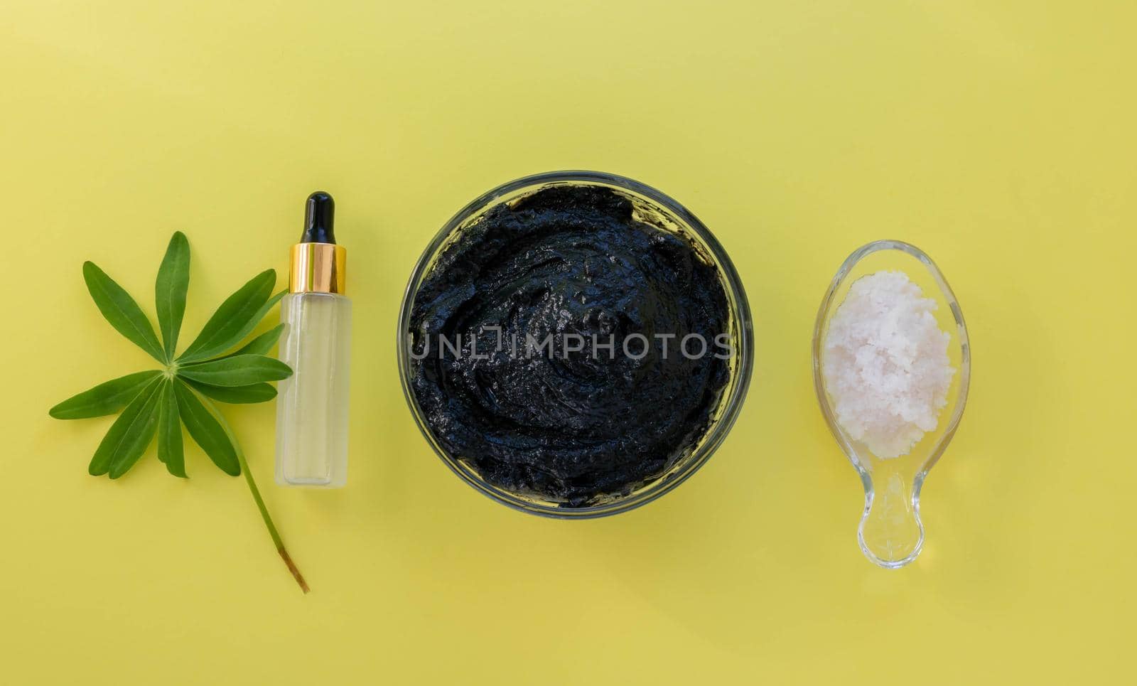 Image of the ingredients of home cosmetics. Black mask, black dirt, pink salt, a bottle with an eyedropper on a yellow background.Skin Care Concept.