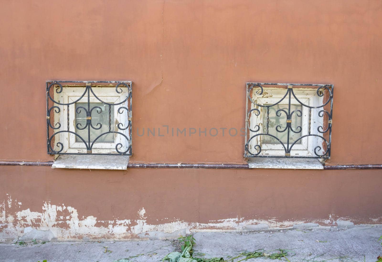 Two windows with antique bars on the plinth .Red facade with small windows.