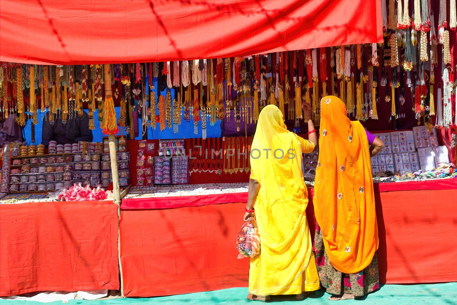Couple of unidentified women in traditional hindu wear saree buying or shopping jewelery items in the commercial street of Pushkar fair in state of Rajasthan, India. Colorful Indian culture concept by arpanbhatia