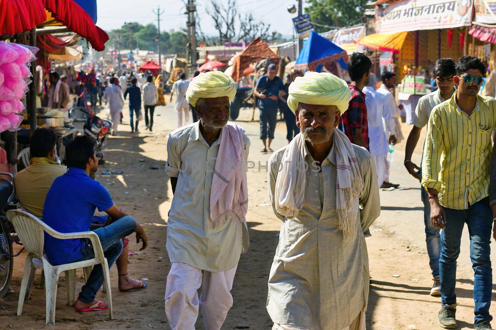 Pushkar, India - November 10, 2016: Couple of local rajasthani old men walking in ethnic wear with turban during famous pushkar fair or mela held annually in Rajasthan state. by arpanbhatia