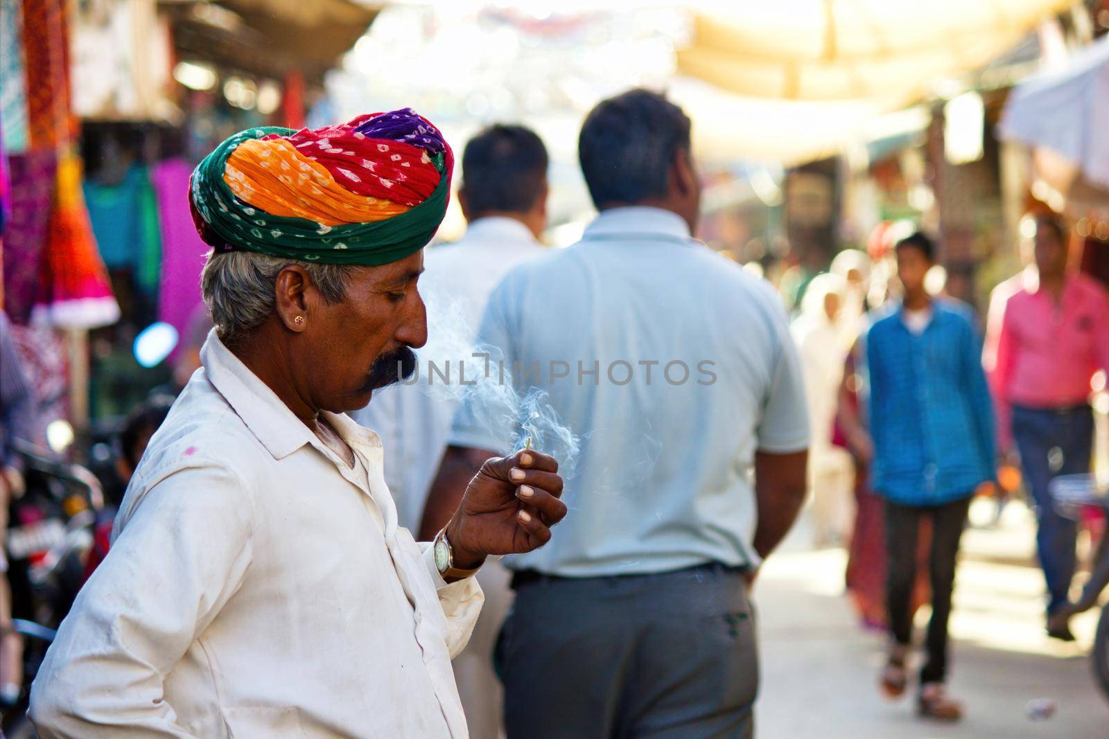 Pushkar, India - NOVEMBER 10, 2016: An old Rajasthani man in traditional ethnic wear such as colorful turban and typical white shirt smoking cigarette or mini-cigar filled with tobacco by arpanbhatia