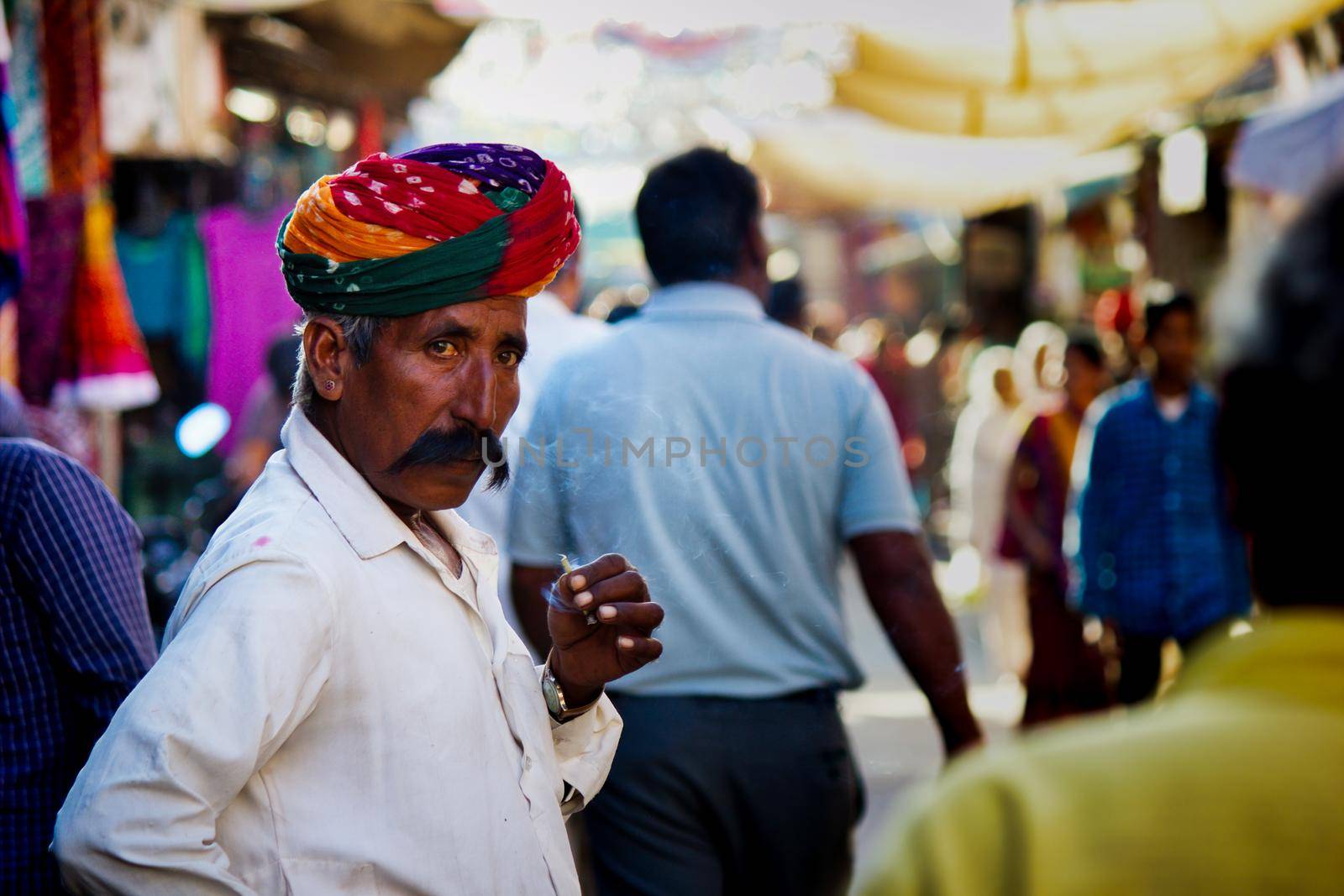 Pushkar, India - NOVEMBER 10, 2016: An old Rajasthani man in traditional ethnic wear such as colorful turban and typical white shirt smoking cigarette or mini-cigar filled with tobacco by arpanbhatia
