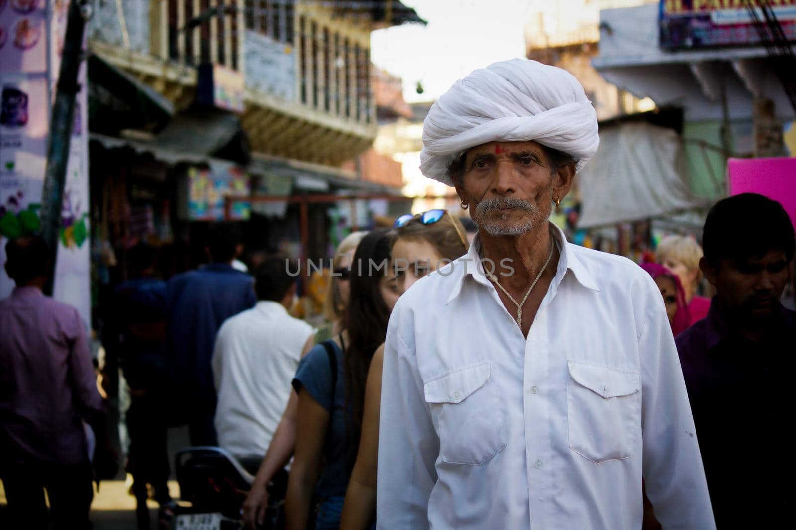 Pushkar, India - November 10, 2016: An old Rajasthani man in traditional ethnic wear such as white turban and typical white kurta walking in a street during pushkar fair in the state of Rajasthan