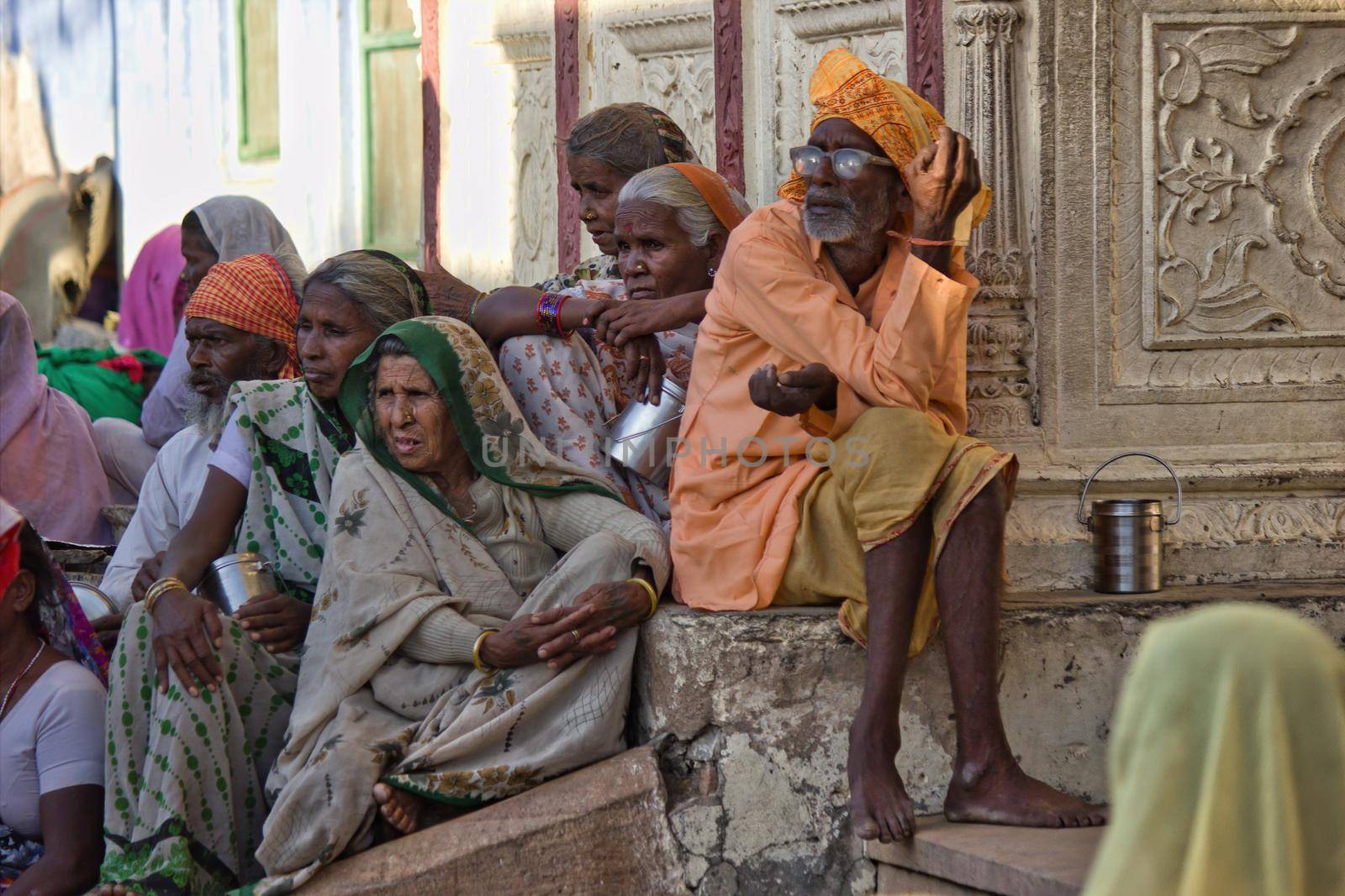 Pushkar, India - November 10, 2016: Bunch of poor people consists of a male with turban and women in saree sitting under the shade waiting for bus in the state of Rajasthan by arpanbhatia