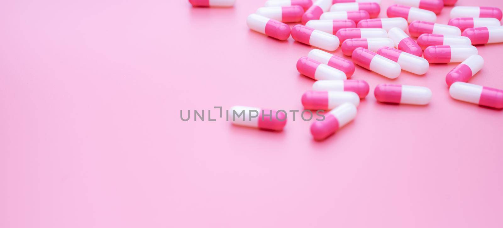 Pink-white antibiotic capsule pills on pink background. Antibiotic drug resistance. Capsule pills spread on pink background. Medication use in hospital. Prescription drugs. Antibiotic drug smart use.