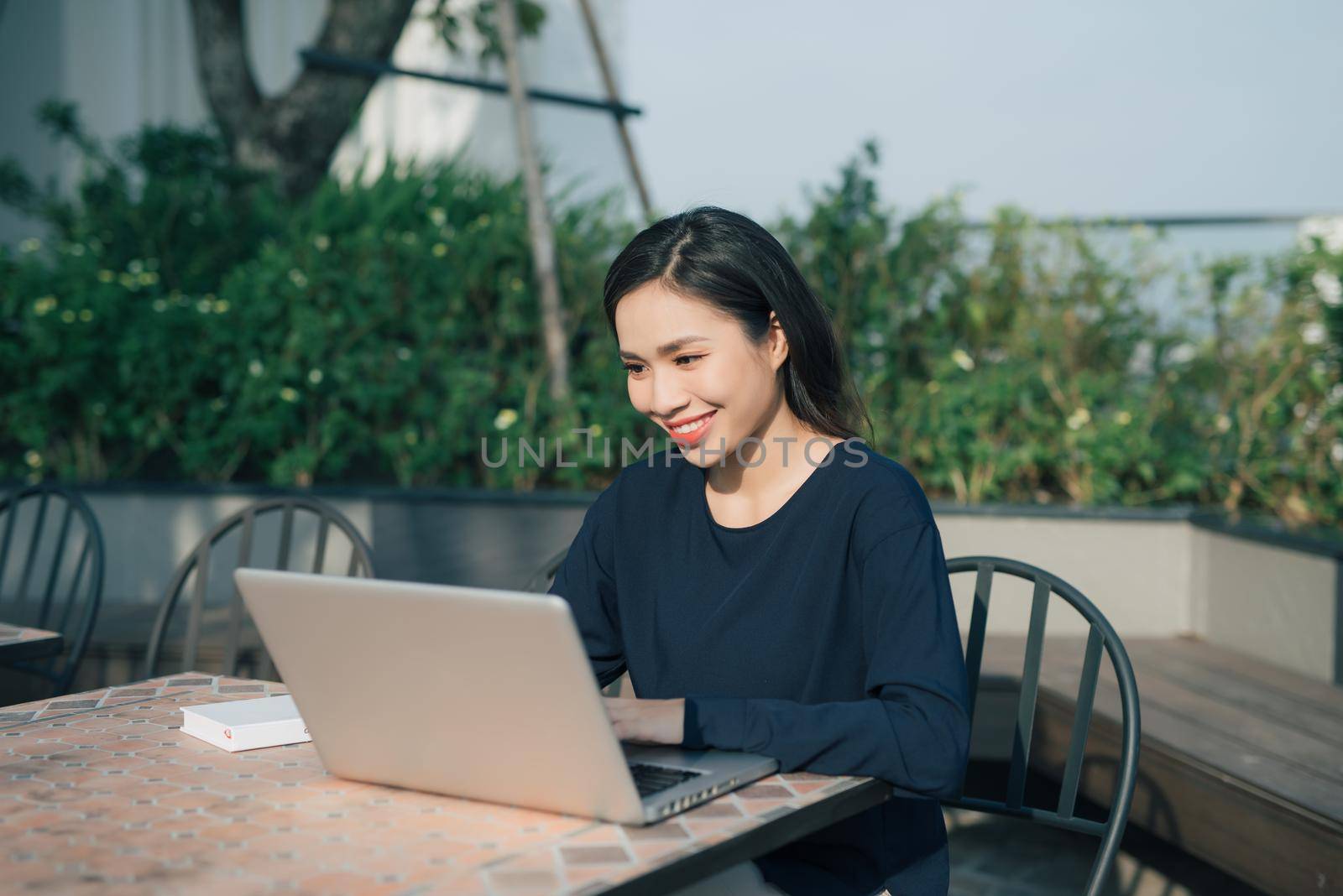 Taking advantages of free Wi-Fi. Beautiful young woman working on laptop and smiling while sitting outdoors by makidotvn