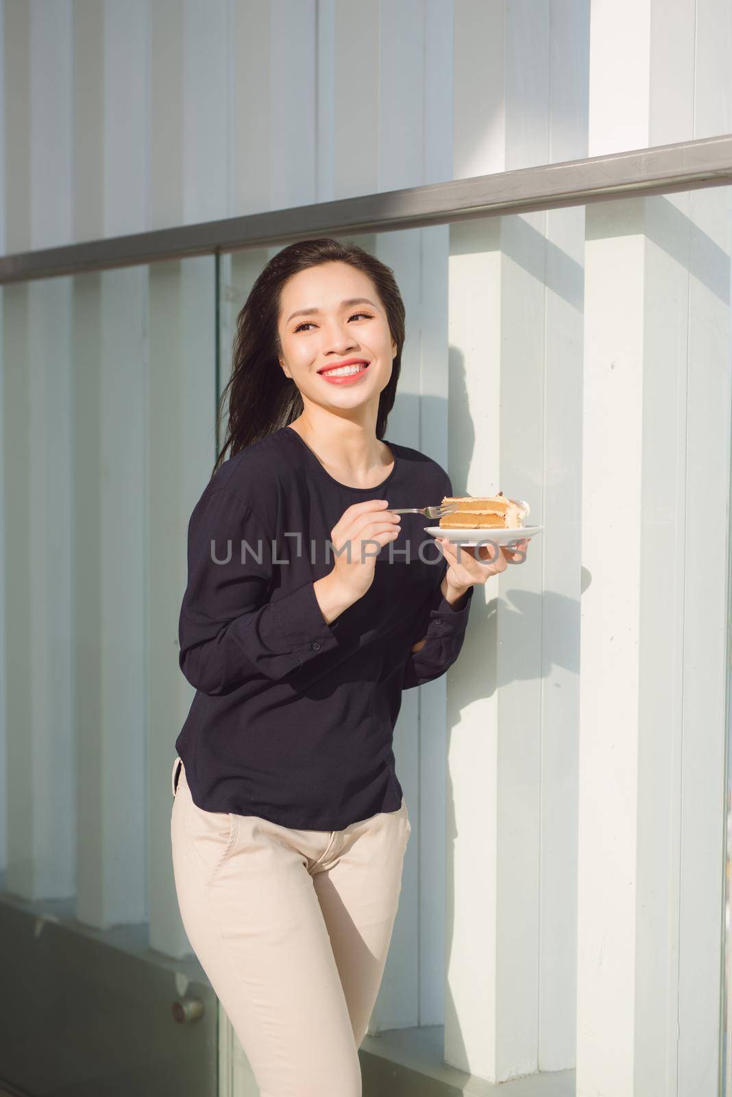 Young happy woman stands on the terrace of the hotel with dish cake in the morning. Pretty asian girl in good mood and is ready for adventures. by makidotvn