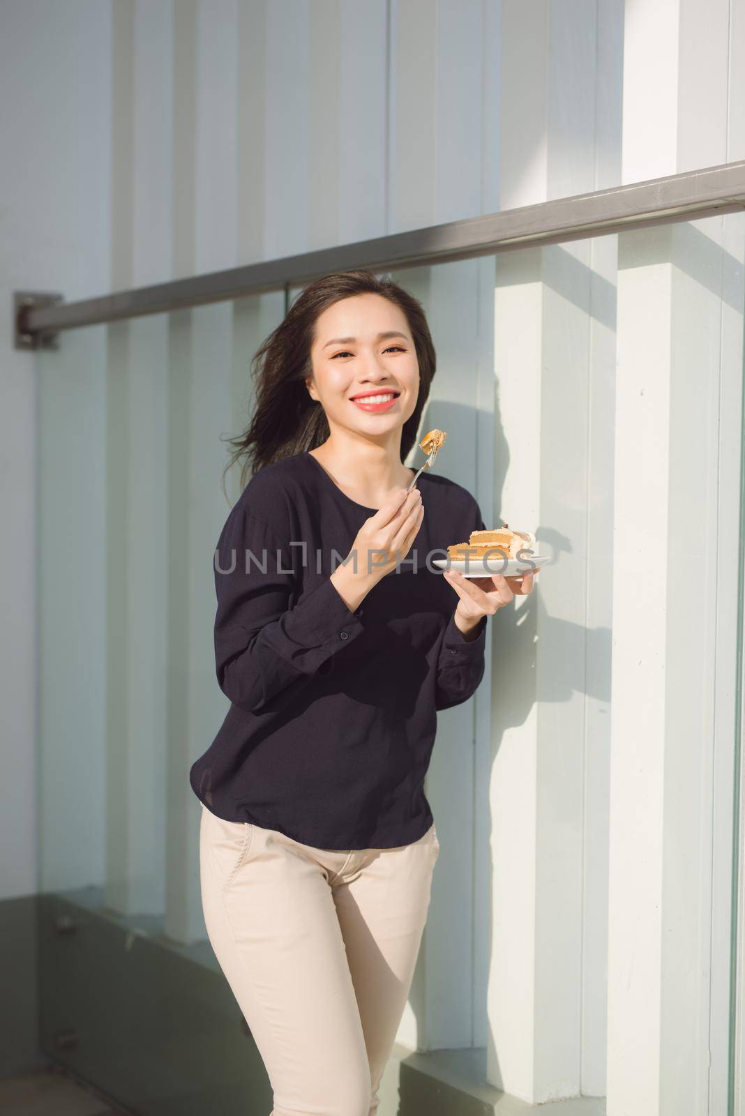 Young happy woman stands on the terrace of the hotel with dish cake in the morning. Pretty asian girl in good mood and is ready for adventures. by makidotvn