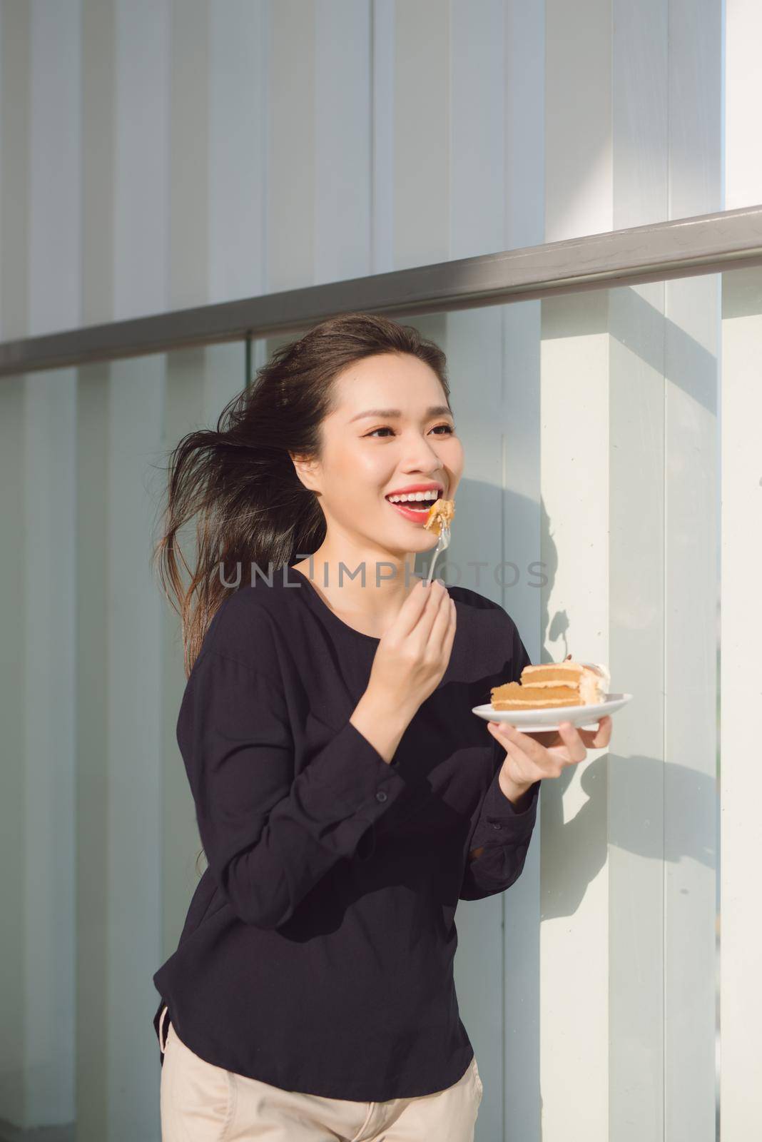 Young happy woman stands on the terrace of the hotel with dish cake in the morning. Pretty asian girl in good mood and is ready for adventures.