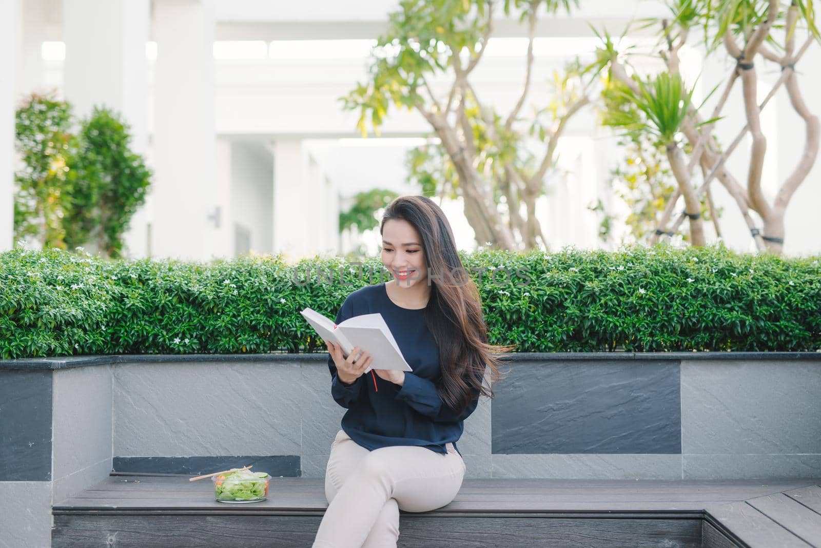 Happy young woman in park on sunny summer day reading book. Cheerful beautiful girl on beautiful day.