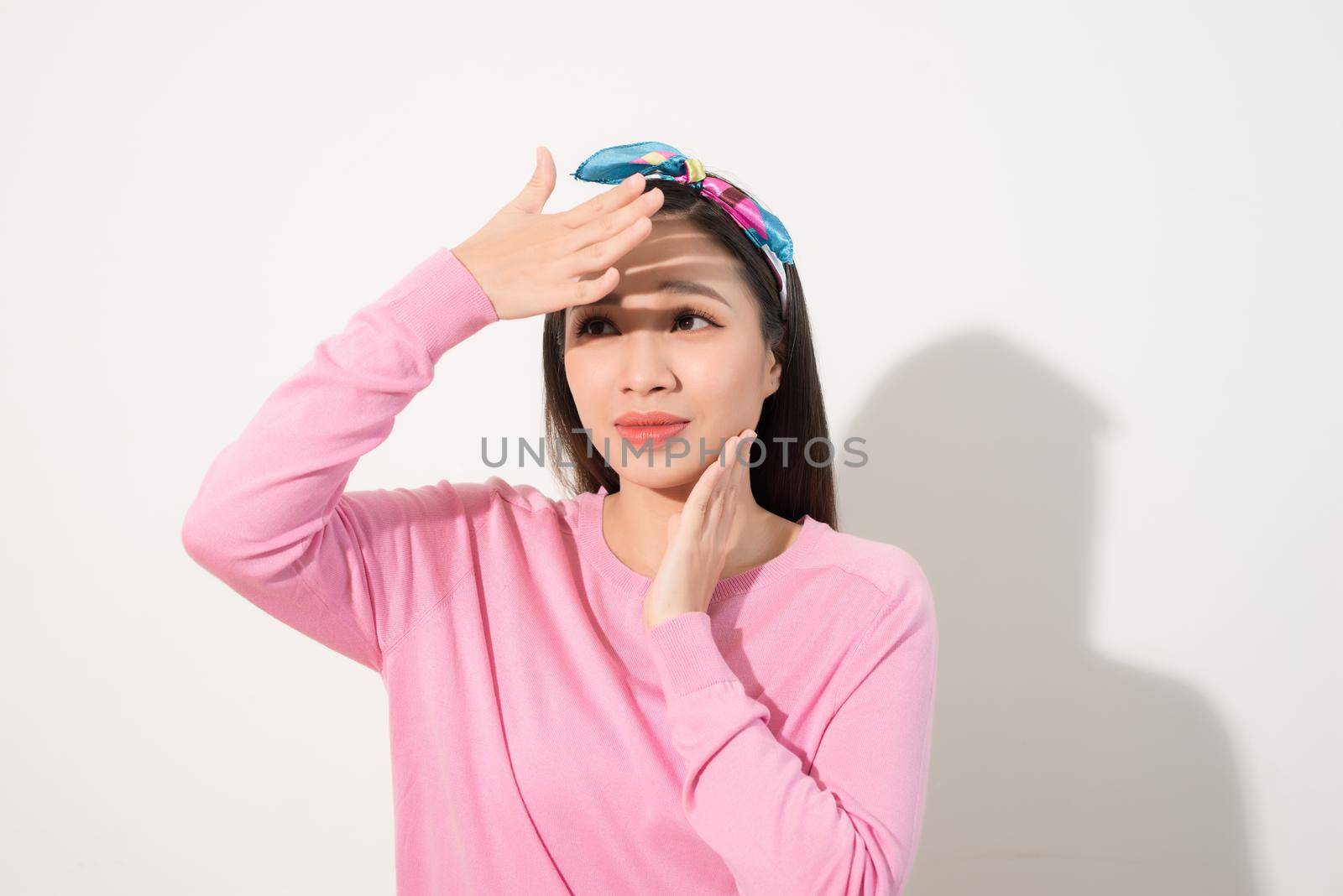 Portrait of a beautiful Asian girl  covering face by hand of bright sun light. Woman in a pink dress protecting her face from solar light. Skin care or beauty concept by makidotvn