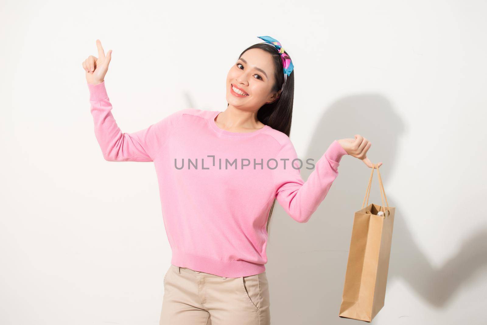 Cheerful young pretty woman raising shopping bags, dancing and looking at camera. Consumerism concept. Isolated front view on white background. by makidotvn