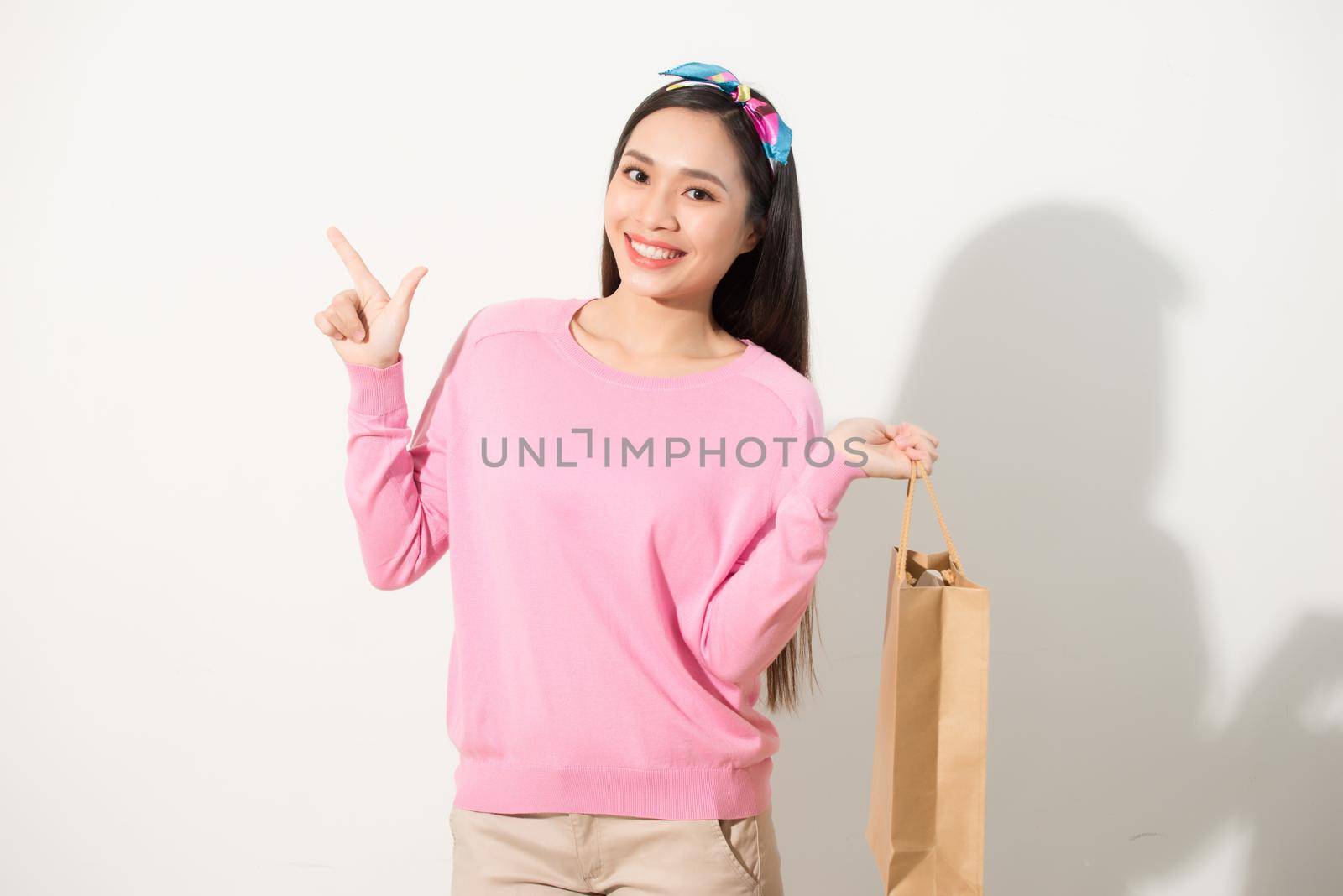 Cheerful young pretty woman raising shopping bags, dancing and looking at camera. Consumerism concept. Isolated front view on white background.