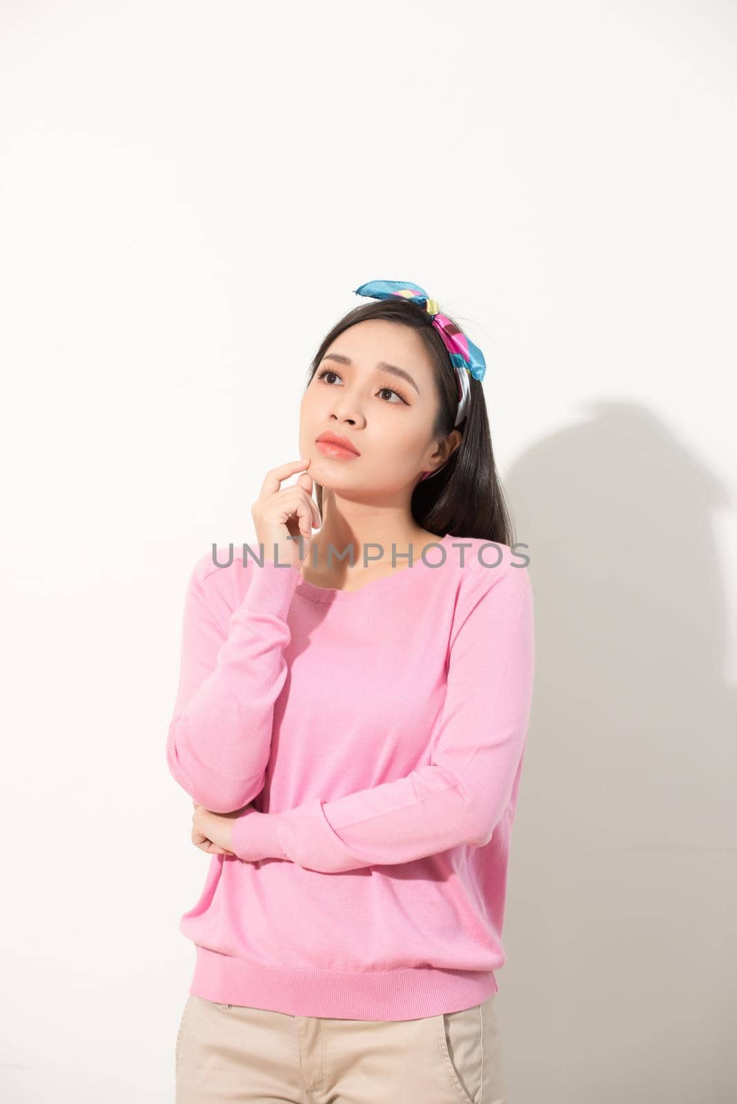 Portrait of a thoughtful young asian woman looking up at copy space with hand on her chin isolated over white background