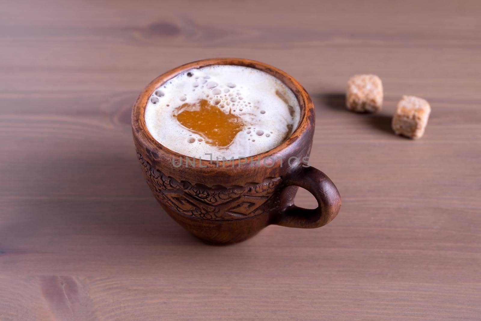 Coffee with milk in a fired earthenware mug with cane sugar pieces by OlgaGubskaya