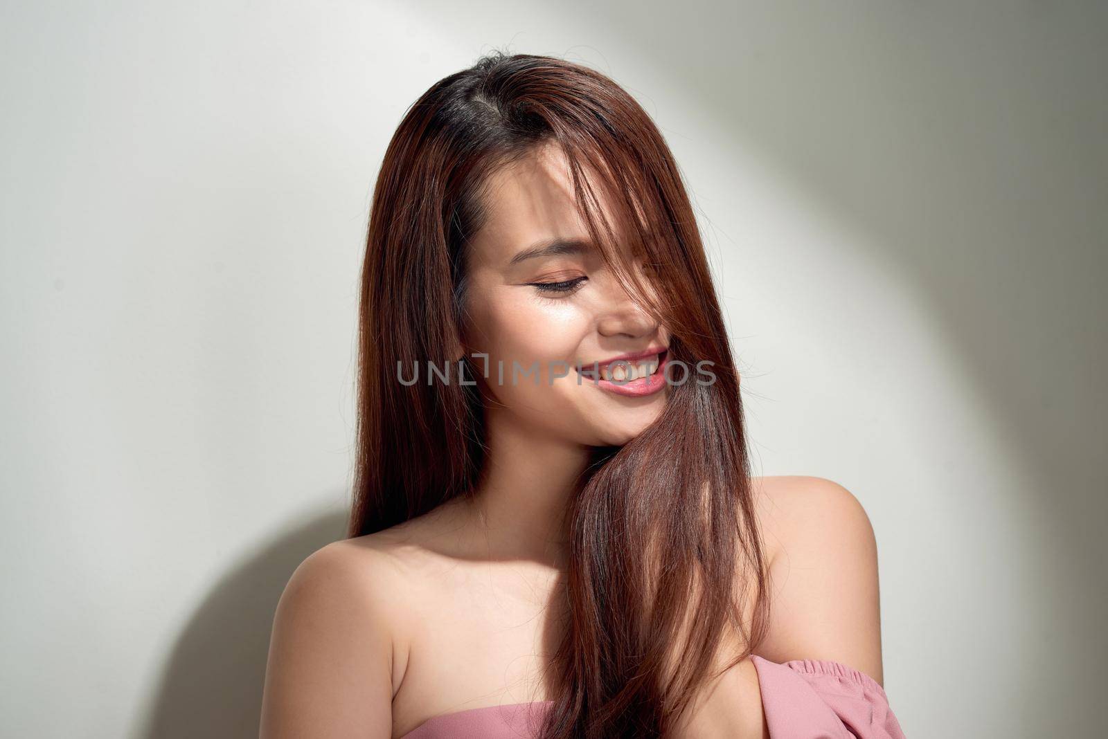 Romantic long-haired girl in trendy dress posing with shy smile. Indoor photo of graceful young woman in summer attire.