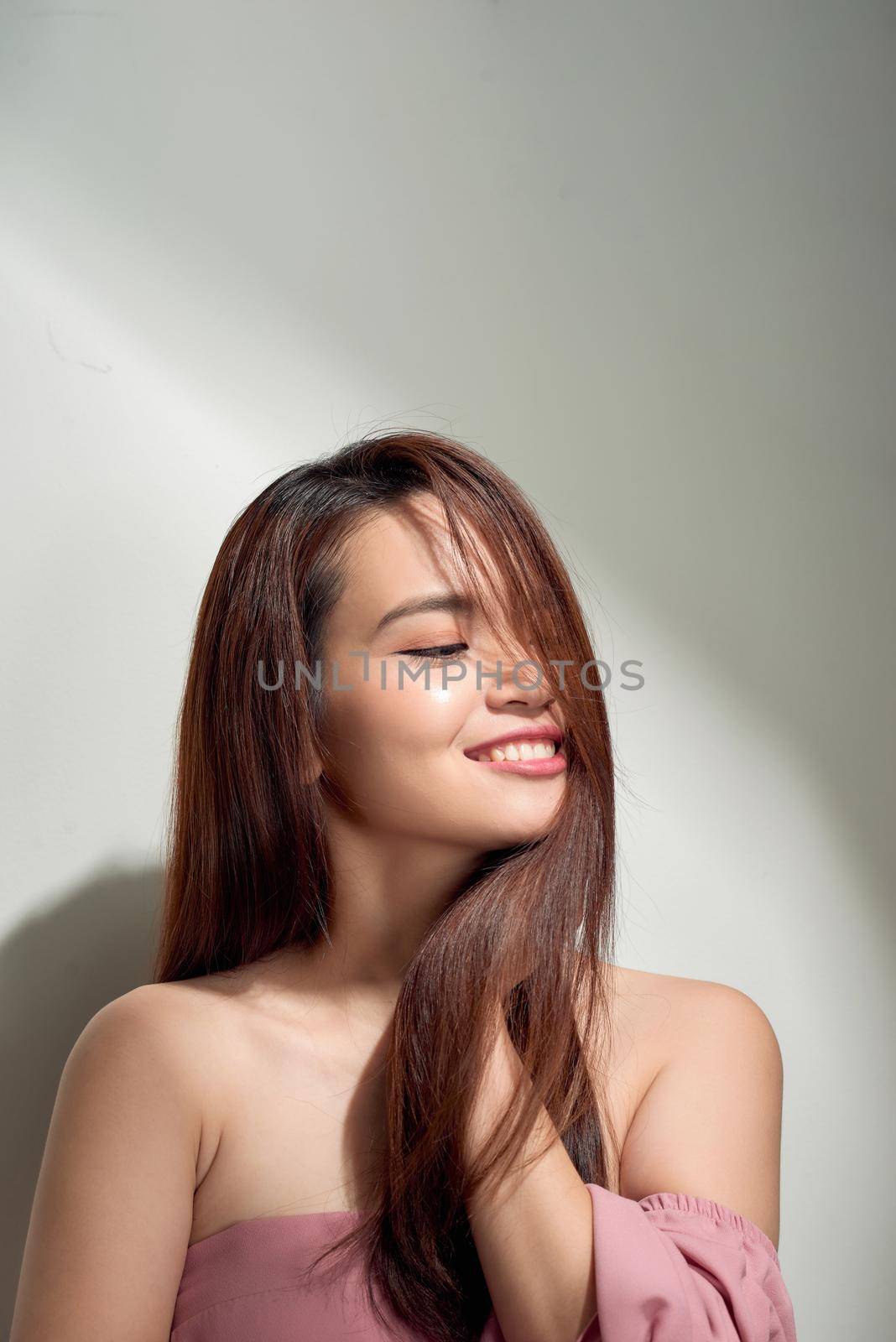 Romantic long-haired girl in trendy dress posing with shy smile. Indoor photo of graceful young woman in summer attire.