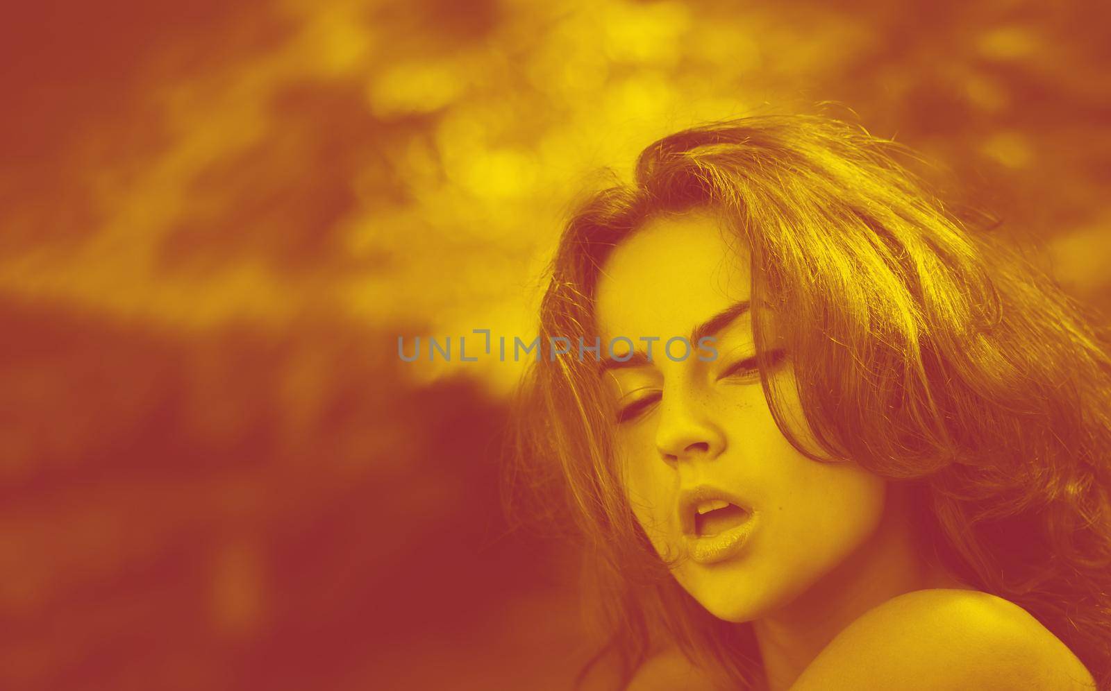 Duotone yellow and red portrait of an emotional young woman against blured nature background of autumn forest.