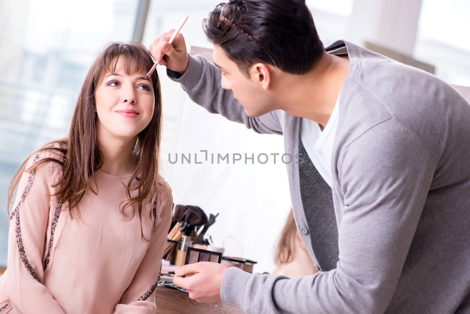 Man doing make-up for cute woman in beauty salon