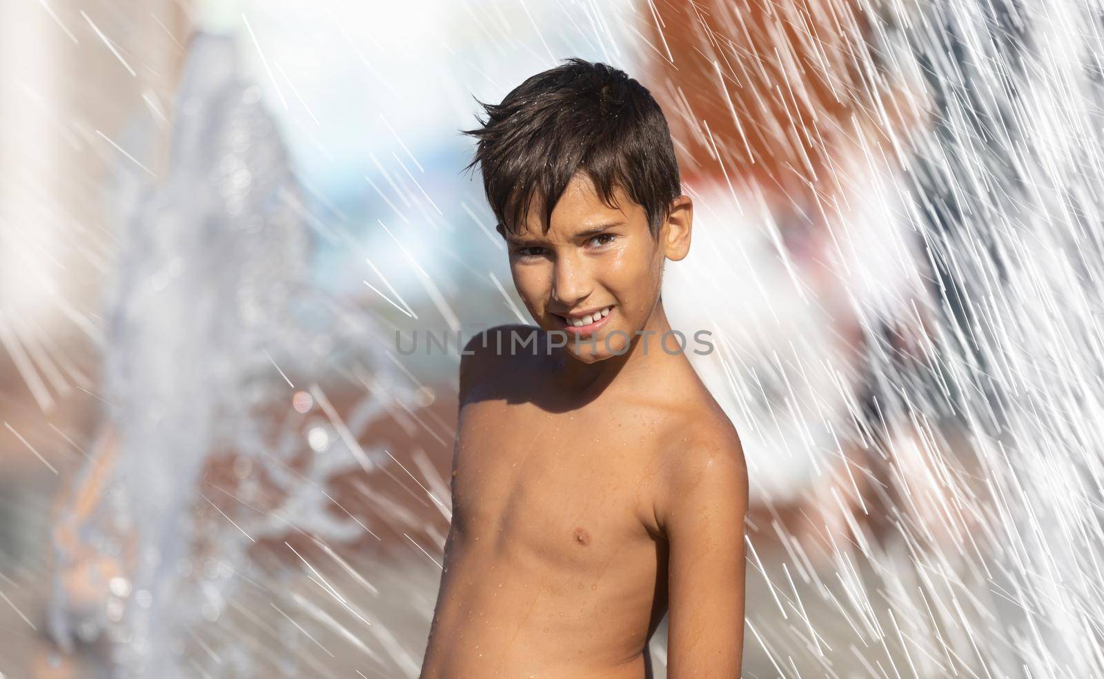 11 years old happy boy playing in a water fountain and enjoying the cool streams of water in a hot day. Hot summer.