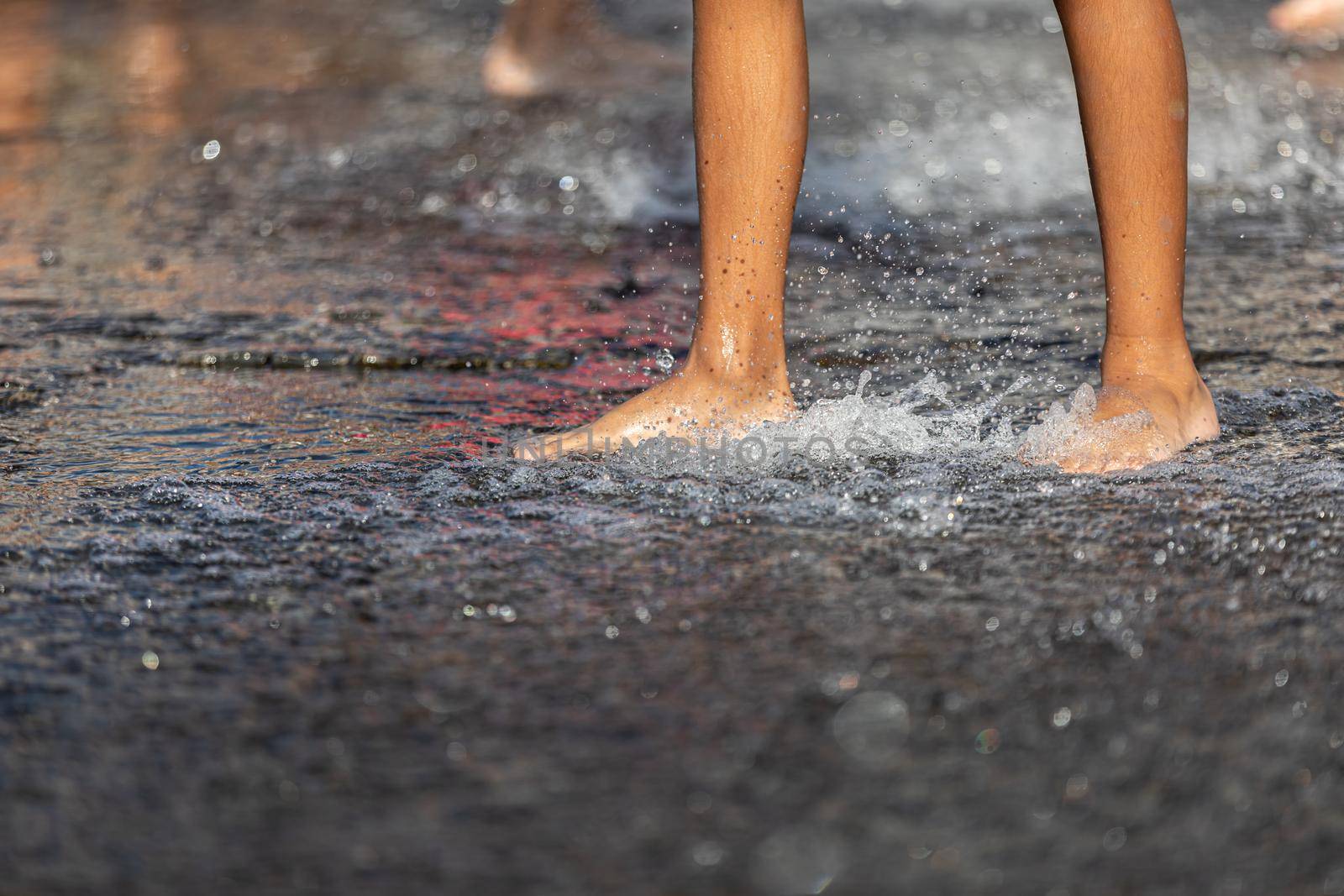 Happy children playing in a water fountain in a hot day. Close-up of children legs in a fountain