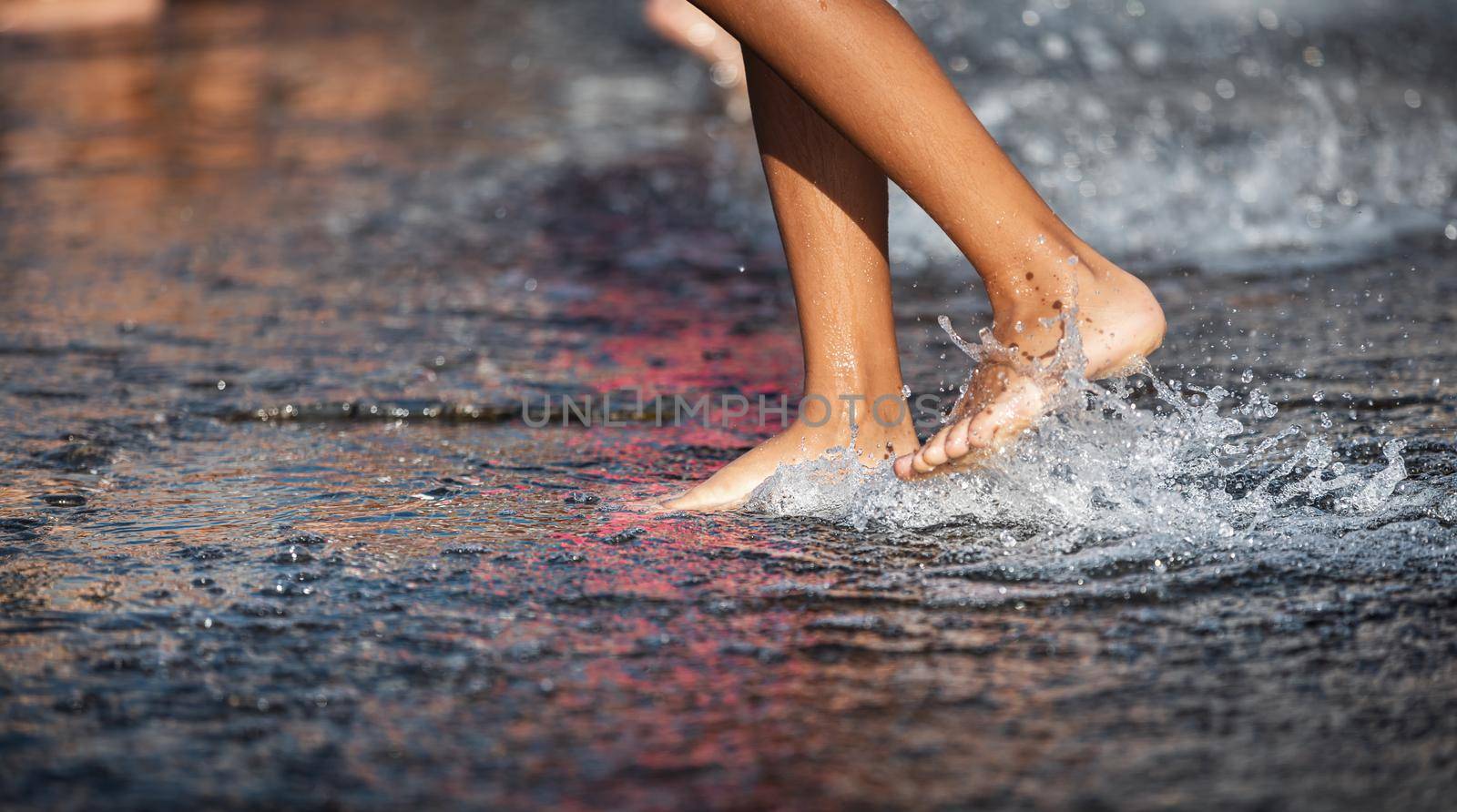 Happy children playing in a water fountain in a hot day. Close-up of children legs in a fountain