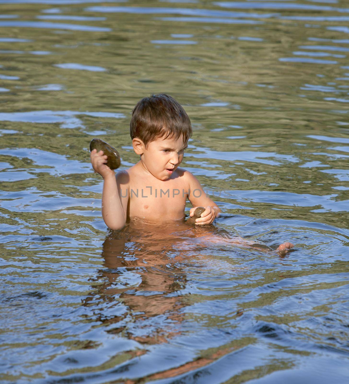 Boy sits in the river and played with a stone